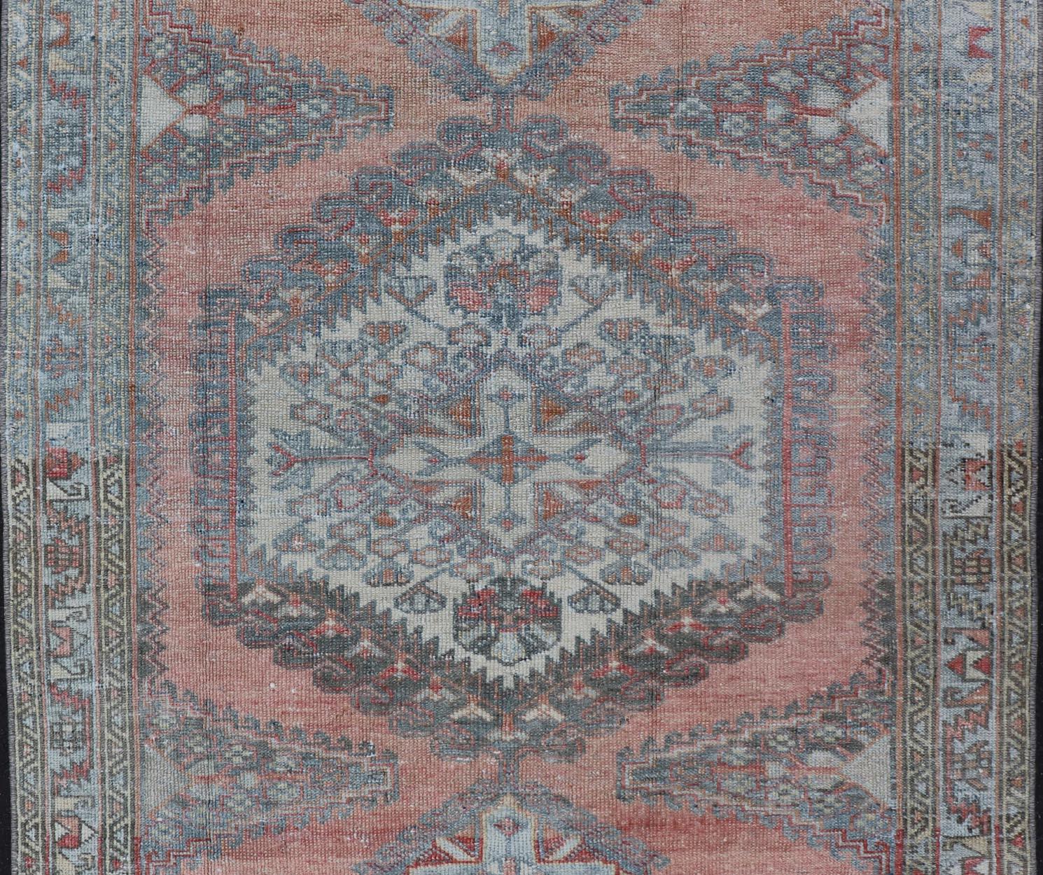 This vintage hand-knotted Persian Hamadan rug features a sub-geometric medallion design enclosed within a complementary, multi-tiered border. The rug has a bold design, however the piece is rendered in soft tones of salmon, blue and gray; making