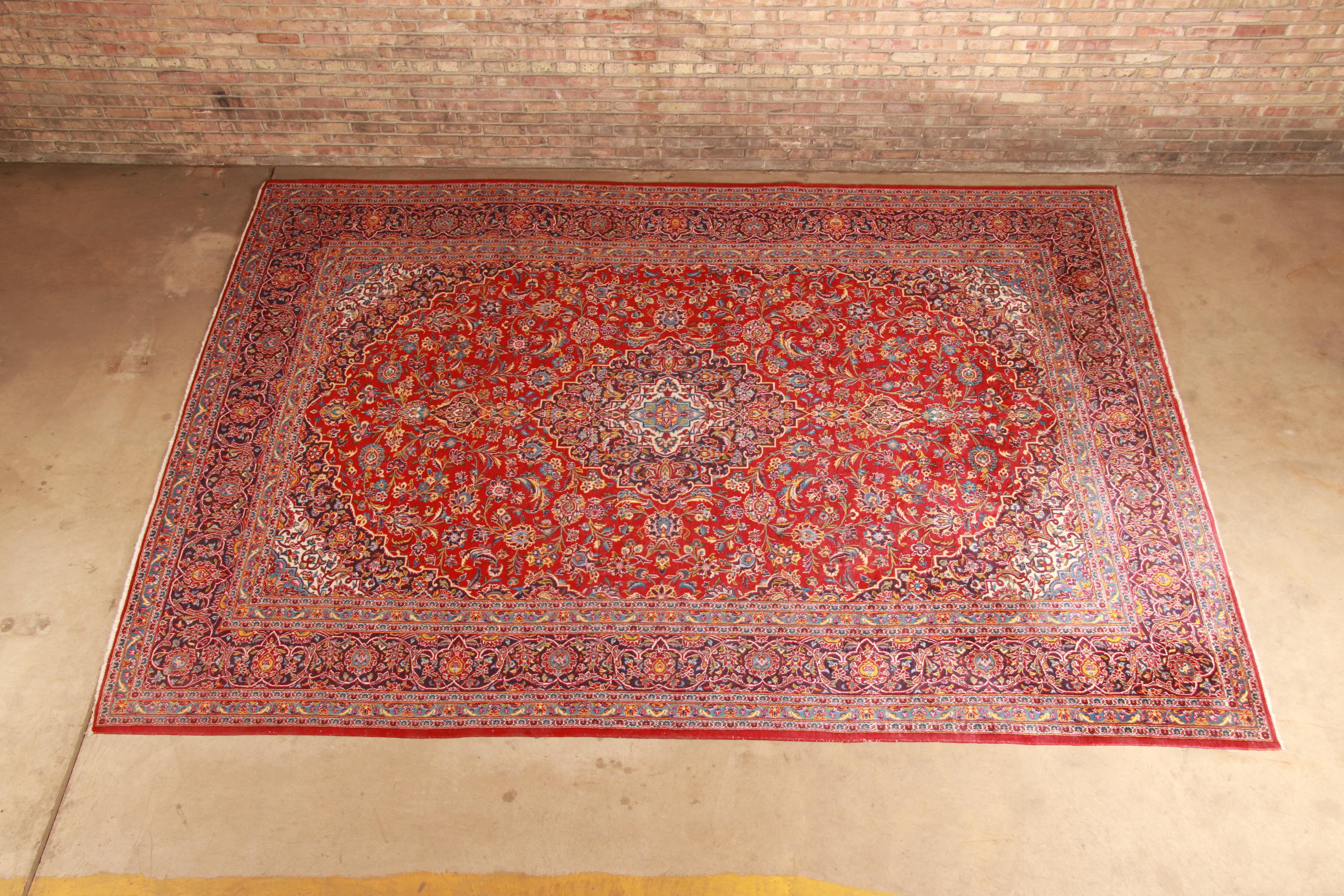 A gorgeous vintage hand knotted Persian Kashan area rug,

20th century

Classic design with floral sprays and bouquets in a red field with center medallion, and rich royal blue border.

Measures: 9
