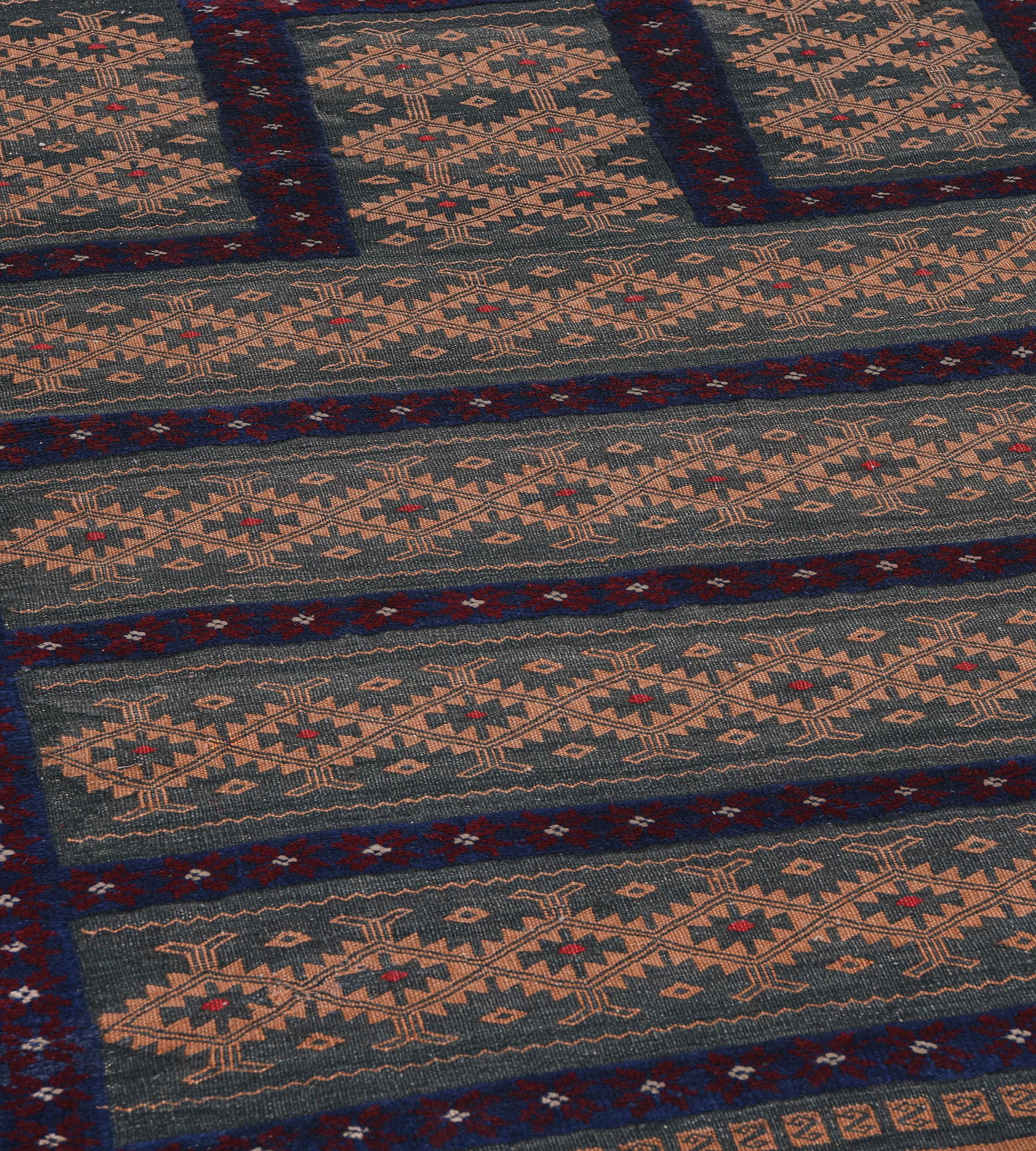 This vintage Persian Balouch flatweave rug has a shaded steel-blue field with five horizontal bands of dusty-pink linked serrated lozenges each with a central steel-blue and tomato-red lozenge, enclosed by an indigo narrow stripe with burgundy-red