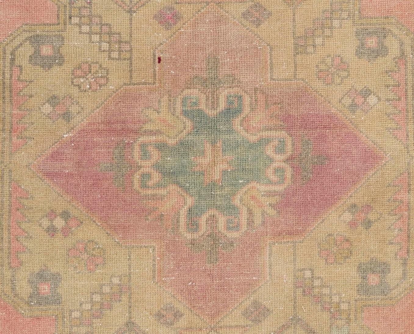 This vintage Turkish area rug features a large medallion design in soft olive green decorated with simpler, more geometric renditions of floral and star motifs that encircle two smaller, nested medallions at the centre in magenta and teal. The rest