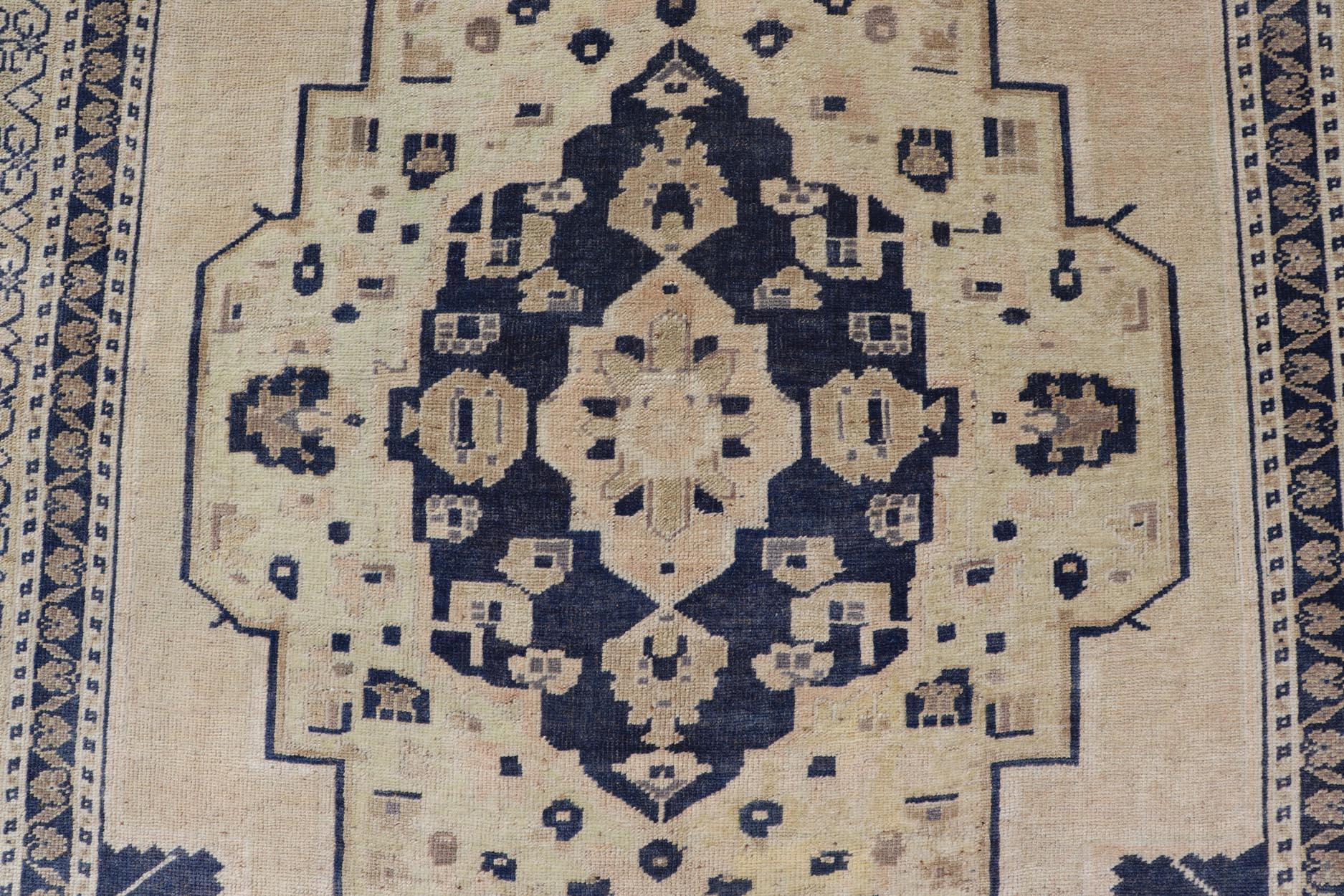 This vintage Turkish Oushak rug has been hand-knotted in wool and features a large central medallion design rendered in blue, cream, tan and ivory tones. A complementary, multi-tiered border encompasses the entirety of the piece; making it a