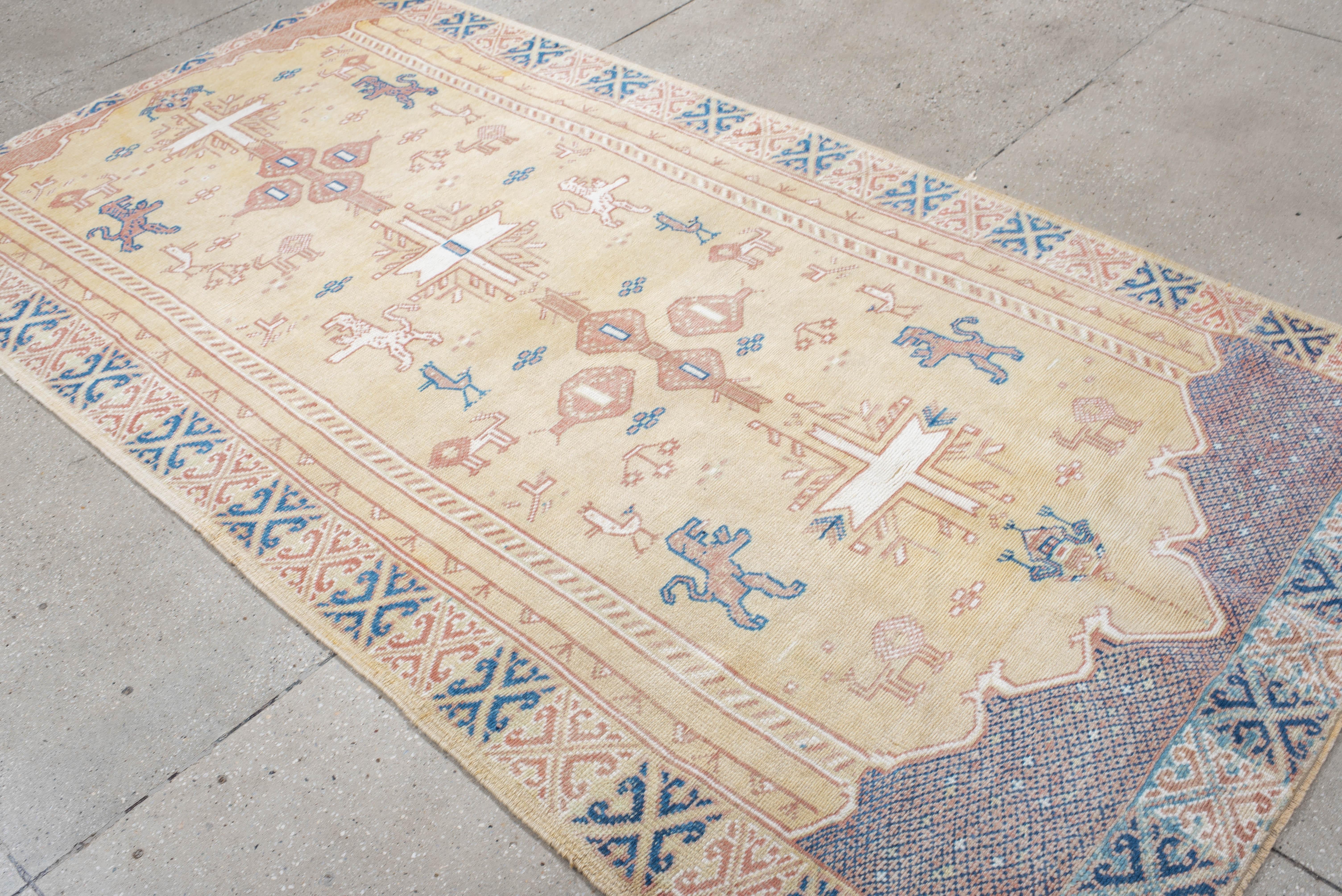 This vintage Turkish rug features stylized animals, geometric medallions, and cross-like forms on a soft tan field. Accents in blush, ivory, and denim blue lend a delicate contrast, framed by detailed borders in traditional Anatolian style.