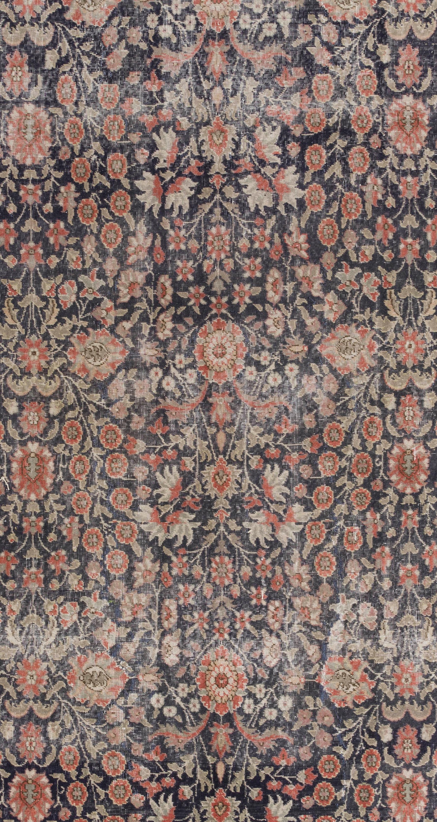 A vintage hand knotted Turkish rug from the 1960s featuring well-drawn and varied floral vines gathering around a few larger-sized rosettes in madder red and olive green with touches of light fawn across the black field. The cream border is filled