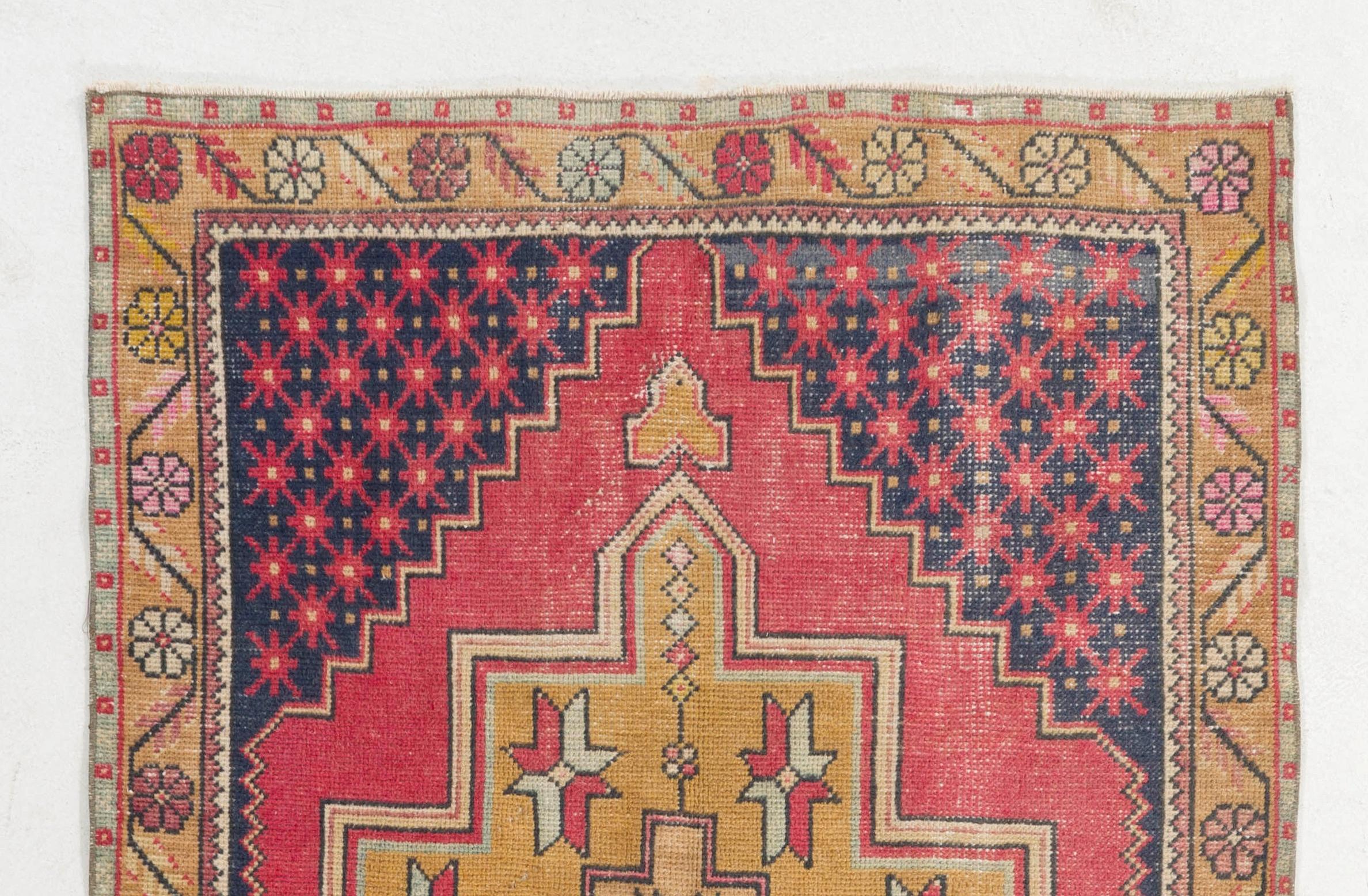 This vintage Central Anatolian area rug has two linked geometric medallions in deep-saturated gold that are decorated with abstract stars against a plain field in vivid raspberry red. The corner-pieces in dark indigo feature a dense pattern of red