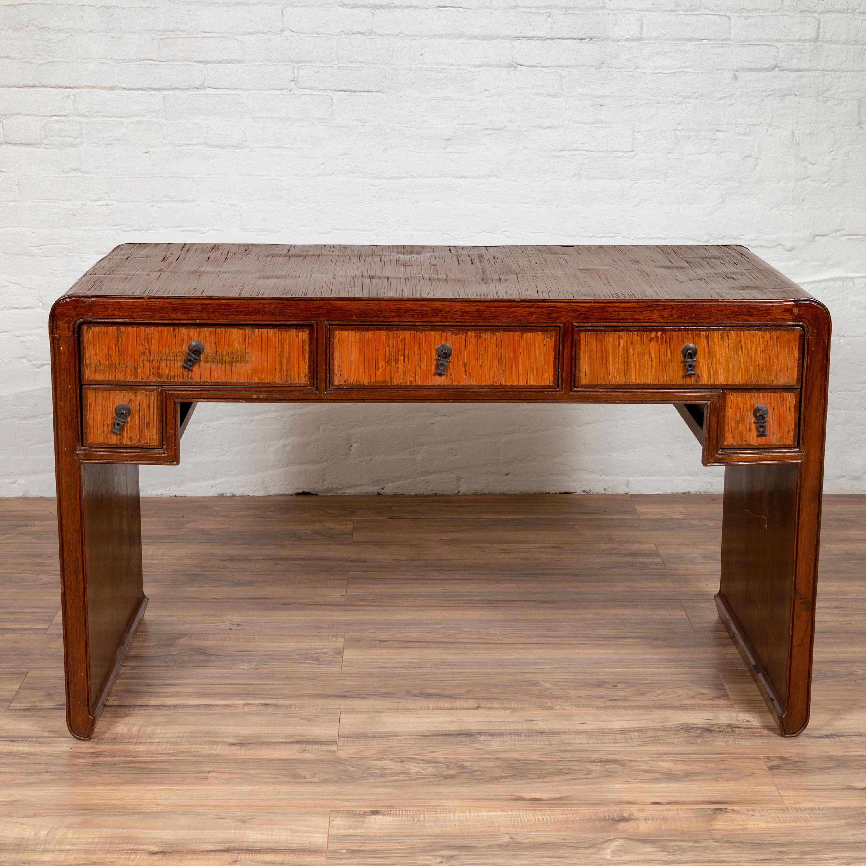 A vintage handmade desk found in Northern Thailand with five drawers and opium mat top. Born in Thailand during the midcentury period, this handmade desk features an opium mat top, flowing delicately into the sides accented with scrolling