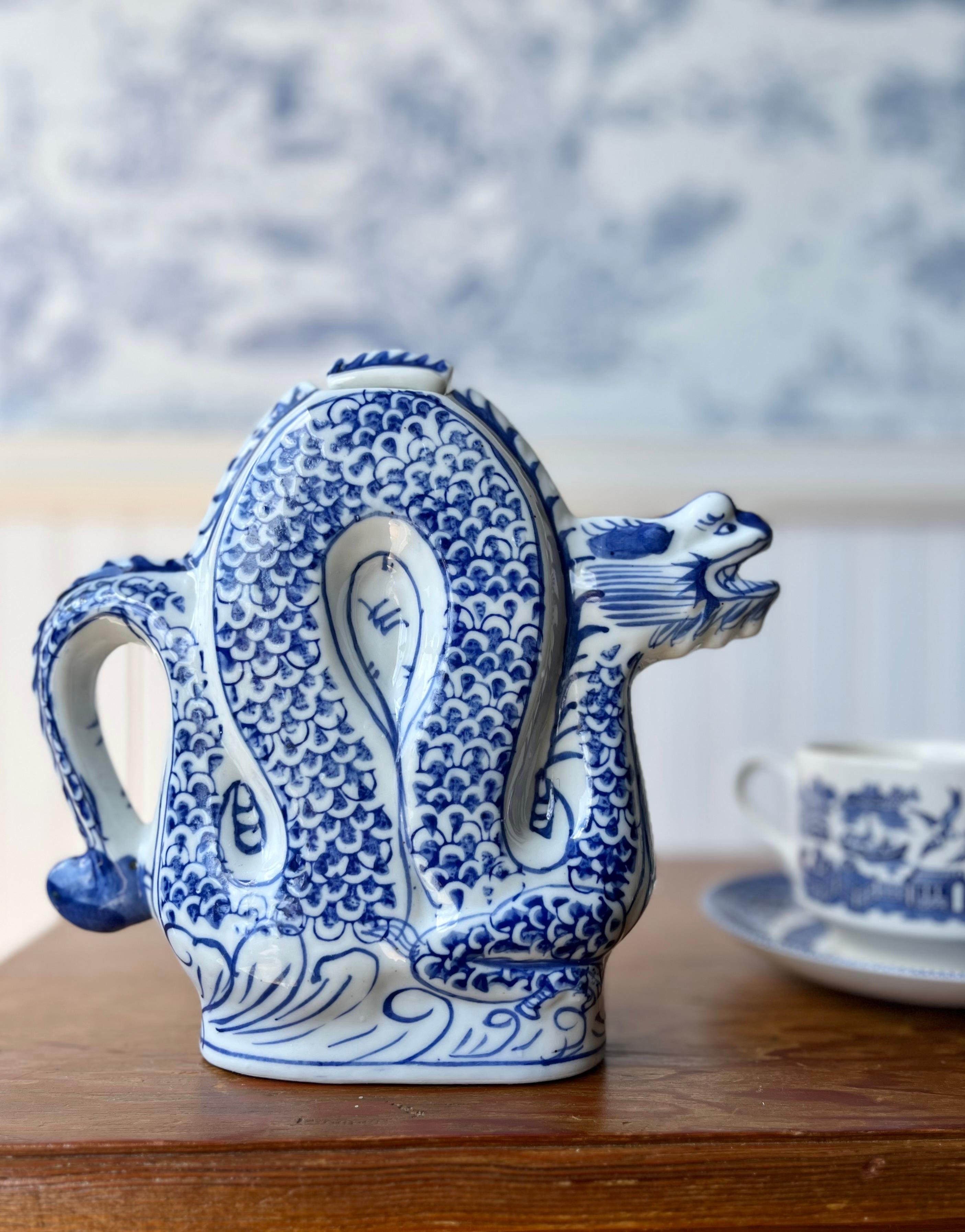 Diese auffällige blau-weiße Porzellankanne in Form eines gewundenen Drachens, dessen Kopf den Ausguss bildet, ist eine skulpturale Ode an die chinesische Kunstfertigkeit. Sie ist in sattem Kobaltblau handbemalt und zeigt traditionelle Schuppenmuster