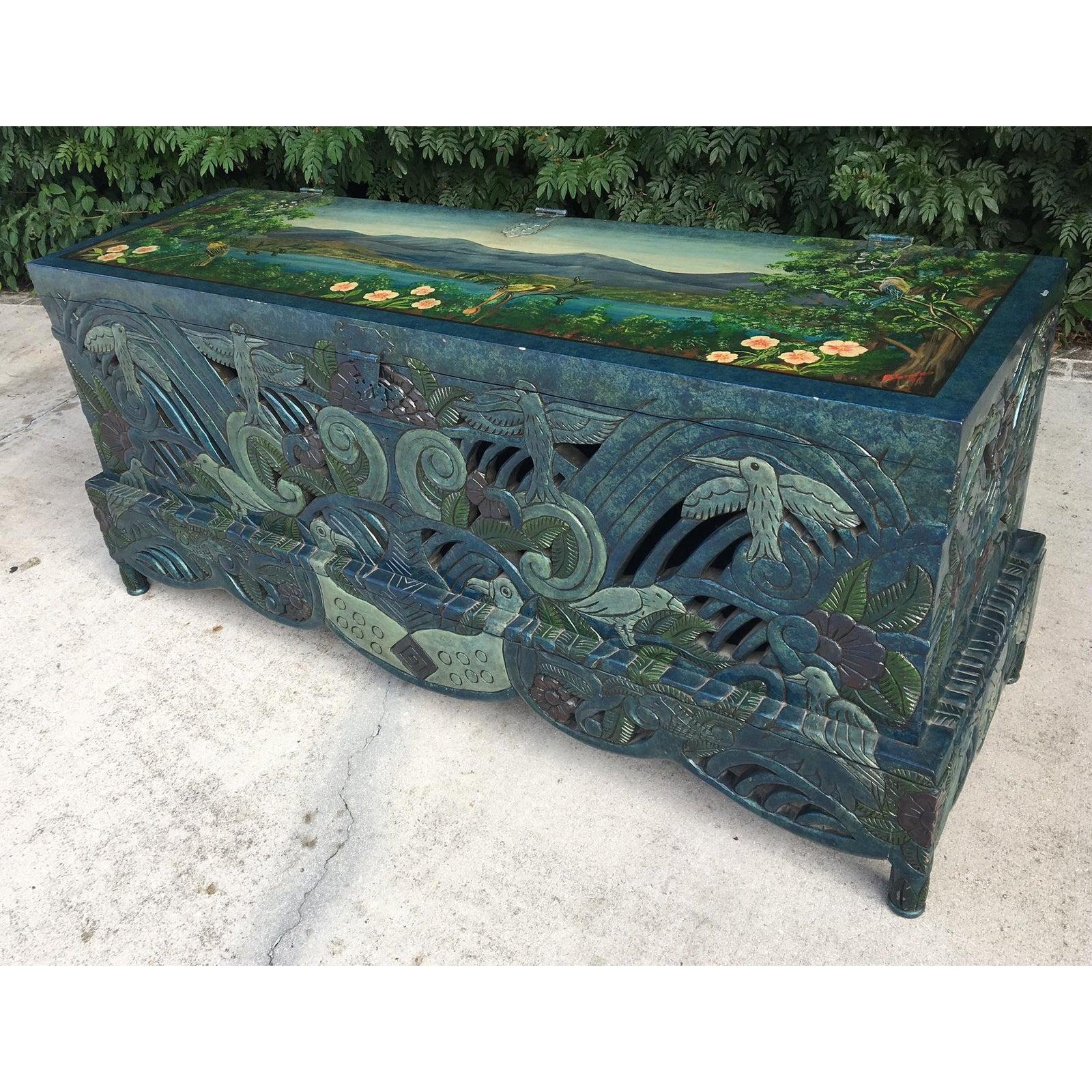 Intricate carving and hand painted detailing throughout make this one-of-a-kind chest a true statement piece. Solid wood construction on an elevated base with ornate hardware. Murals on top and inside featuring tropical birds and flowers by artist