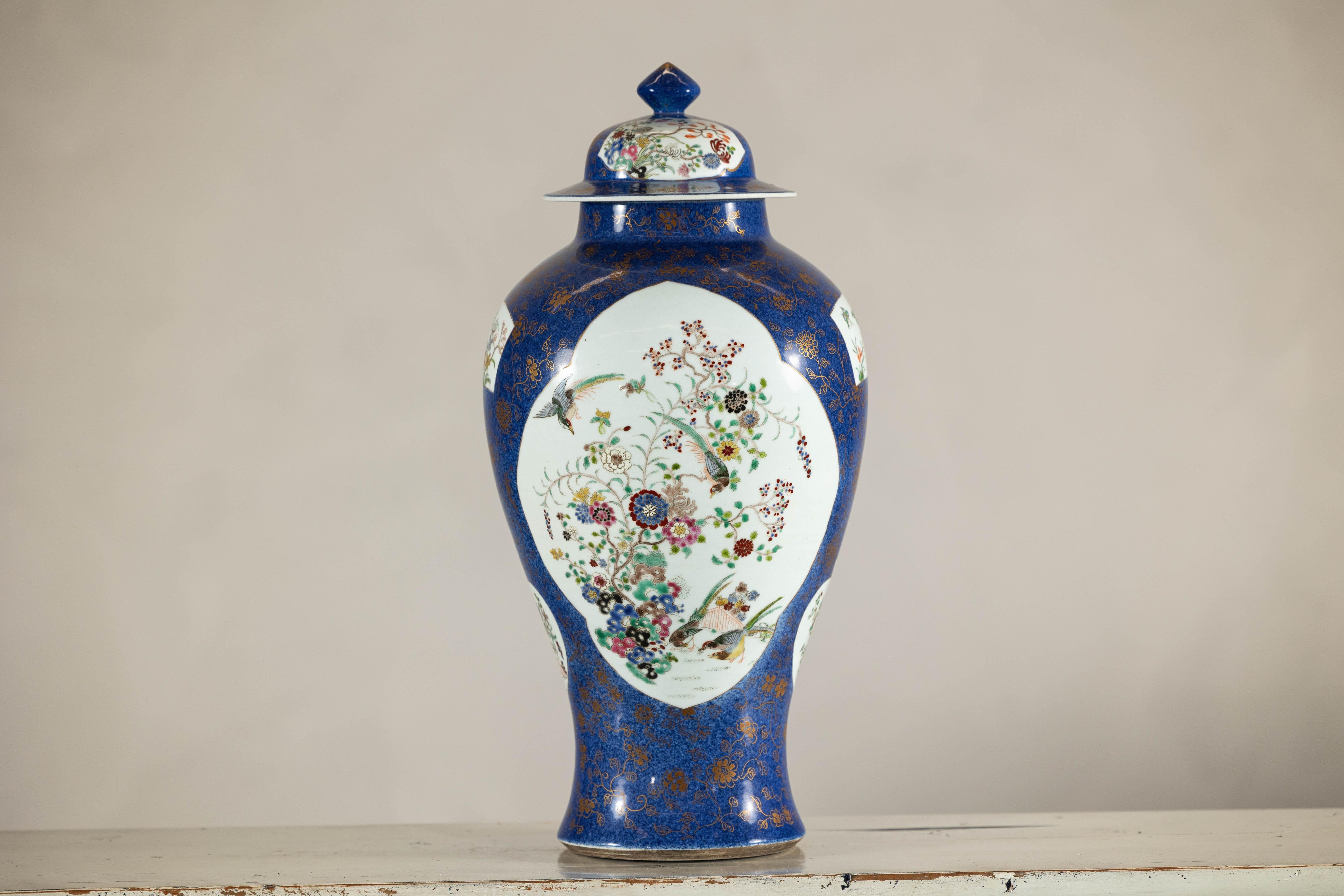 Un pot de gingembre vintage peint à la main sur un fond bleu cobalt saisissant, orné de motifs floraux dorés complexes et de panneaux traditionnels de style famille rose. Cette pièce en porcelaine du XXe siècle présente une forme de balustre, sa