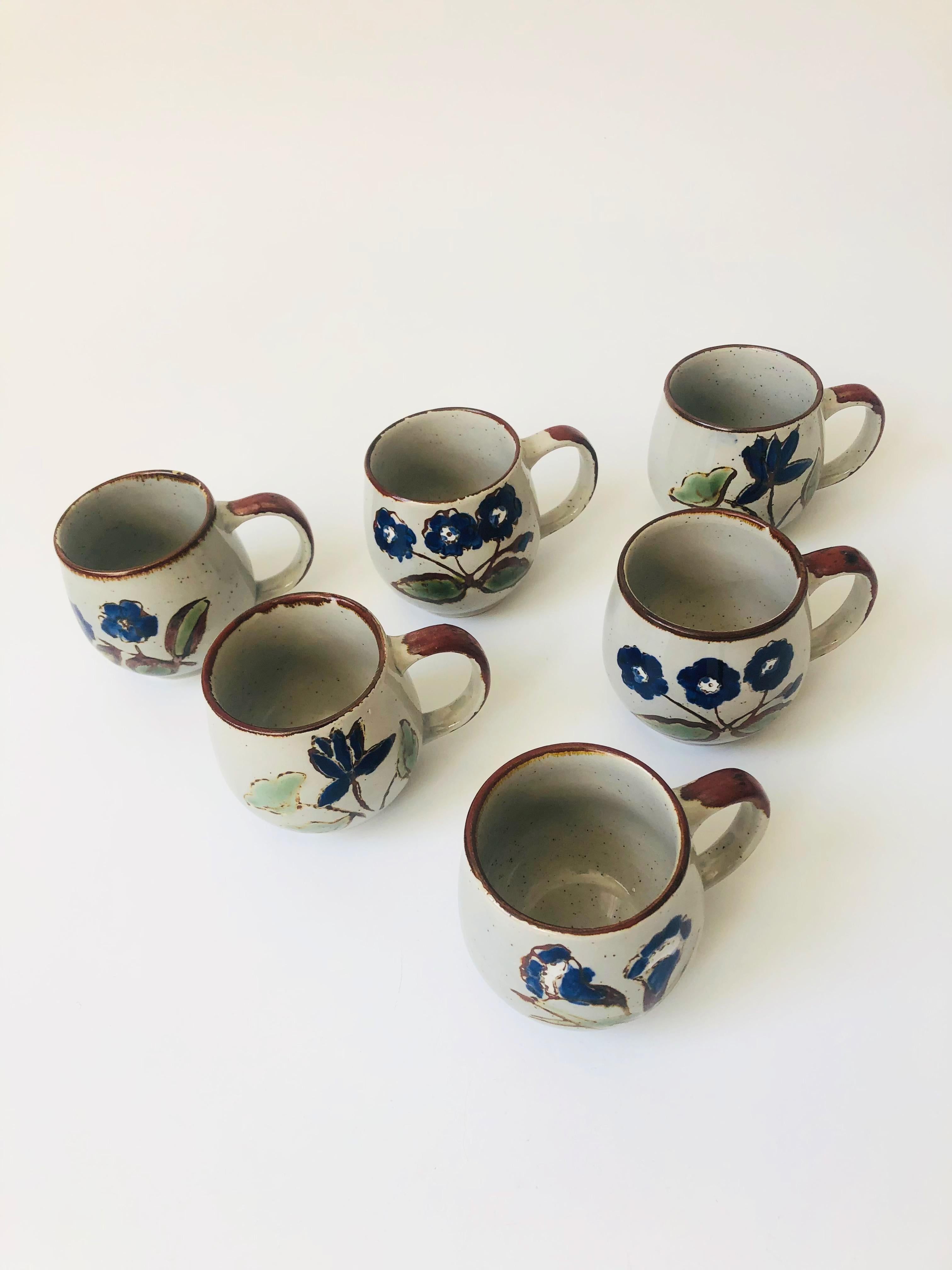 Ein Satz von 6 alten Tassen aus Keramik. Jedes Stück weist ein süßes, handgemaltes blaues Blumenmuster auf einer gesprenkelten grauen Grundfarbe auf.
 