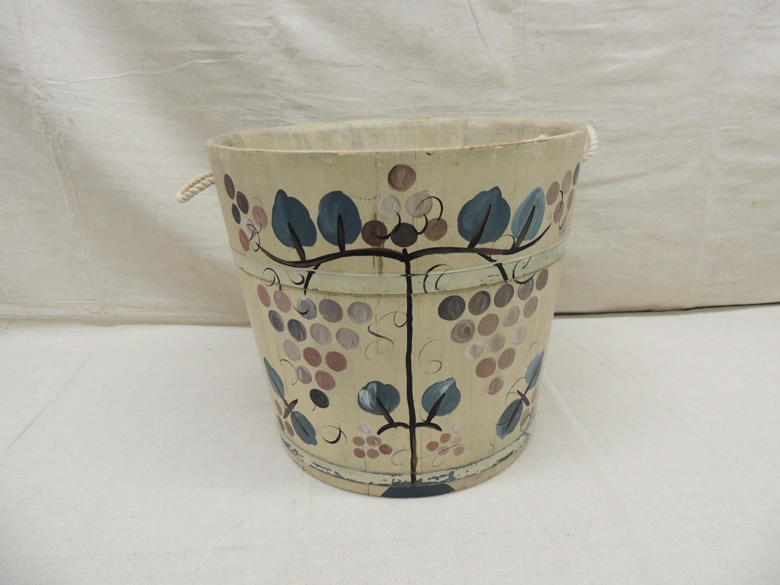 Vintage Handpainted Folk Art Style bucket with ropes handles
Decoration depicts grapes and vines. In shades of tan, green, mauve, and black
USA, 
Wood, metal, paint and twine rope
Ideal as a wastebasket, magazine rack, fireplace log holders
Folk art
