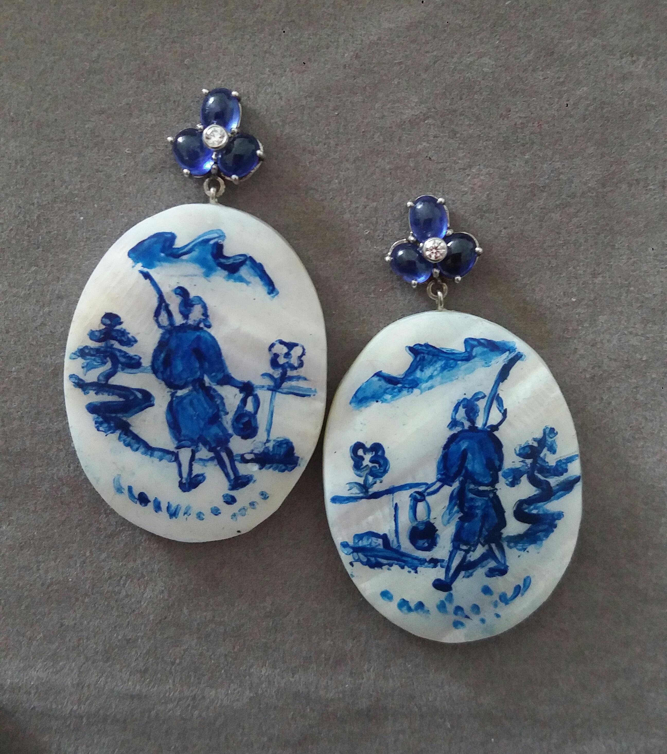 Vintage pair of oval shape hand painted Mother of Pearl 28 mm x 40 mm, depicting a chinese fisherman walking near the river ,suspended from 3 Blue Sapphire cabs each measuring 4x5 mm with a small full cut diamond in the center.

In 1978 our workshop