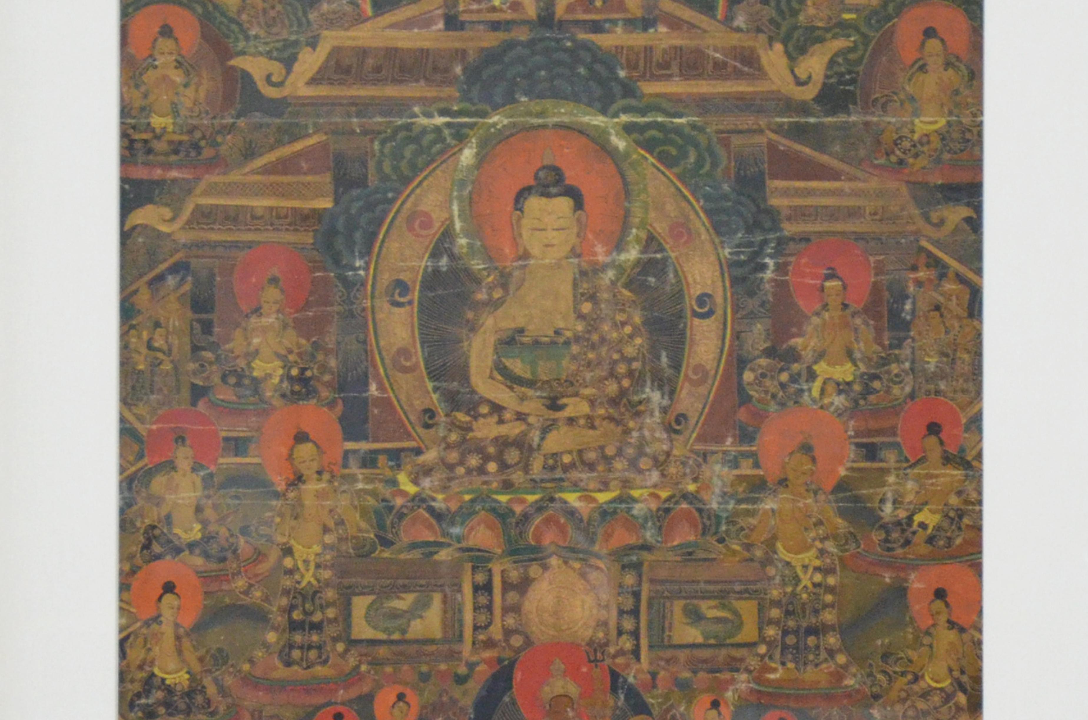A vintage Tibetan hand-painted Thangka painting on canvas depicting the Buddha and multiple deities, in dark brown beveled frame. Created in India during the mid 20th century, this painting on canvas, called a Thangka, showcases a multi-colored