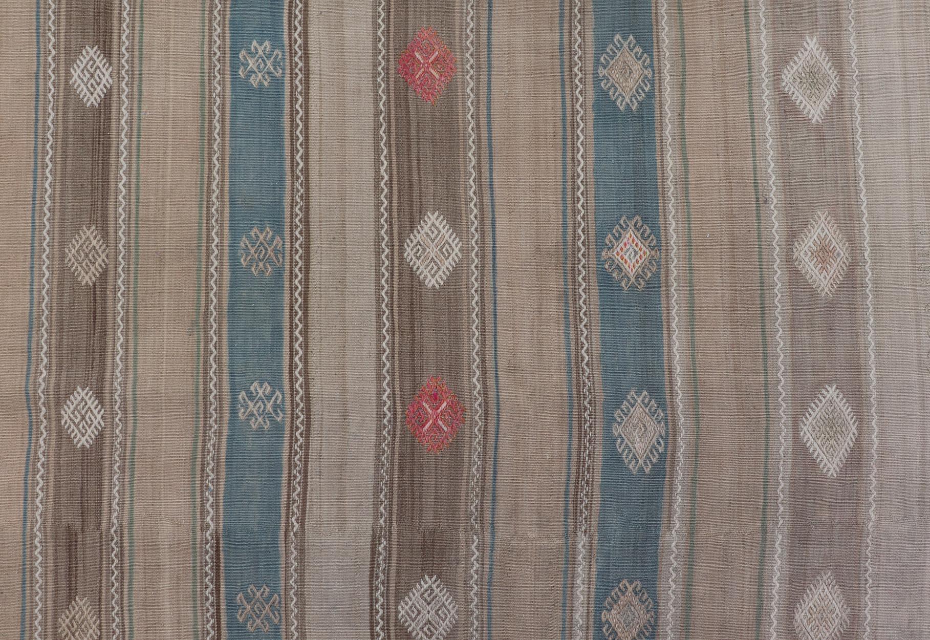 Este kilim tribal de tejido plano se ha tejido a mano en lana. La alfombra presenta un diseño de rayas horizontales, acentuado por varios motivos subgeométricos. La alfombra es multicolor, por lo que encaja perfectamente en una gran variedad de