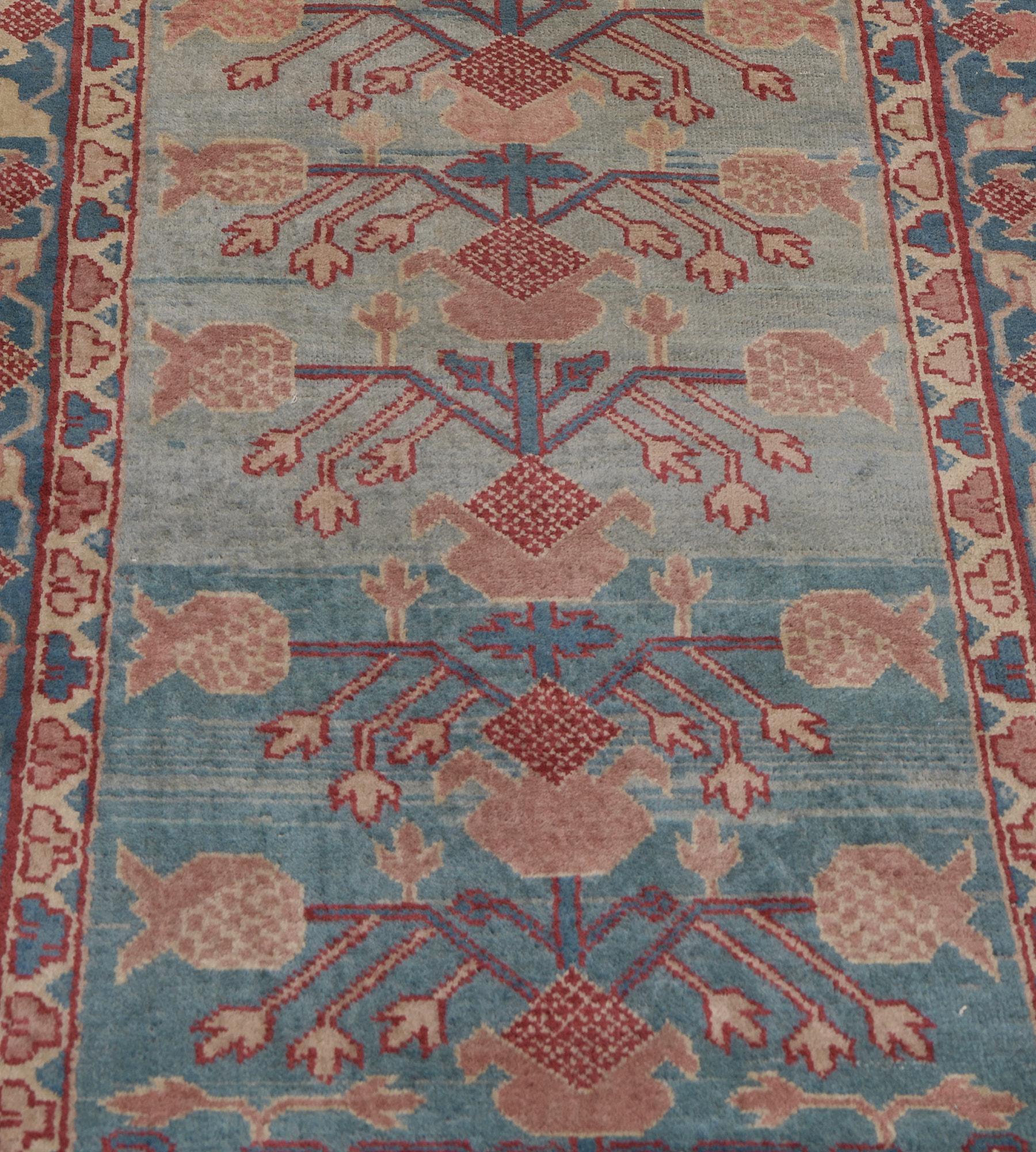 This antique Khotan runner has a shaded sky-blue field with a central column of dusty-pink pomegranate and angular leafy vine issuing further pomegranates, in a shaded mid-blue border of meandering floral vine between ivory barber-pole and floral