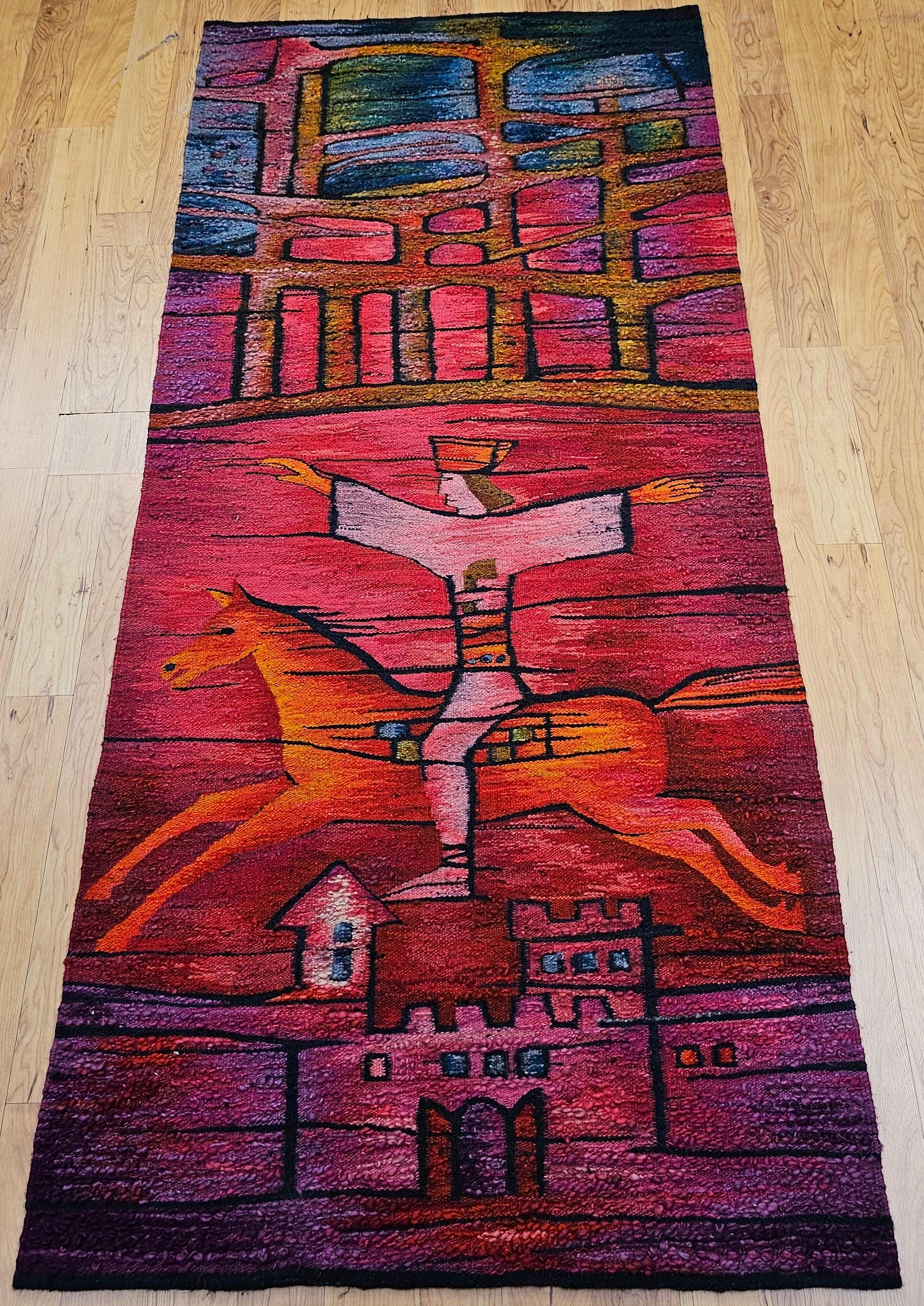 Dieser atemberaubende Wandteppich aus der Mitte des Jahrhunderts zeigt einen folkloristischen Reiter, der auf einem galoppierenden Pferd akrobatische Kunststücke vollführt. Das in juwelenfarbenen Tönen gewebte Werk strahlt Rhythmus, Bewegung und