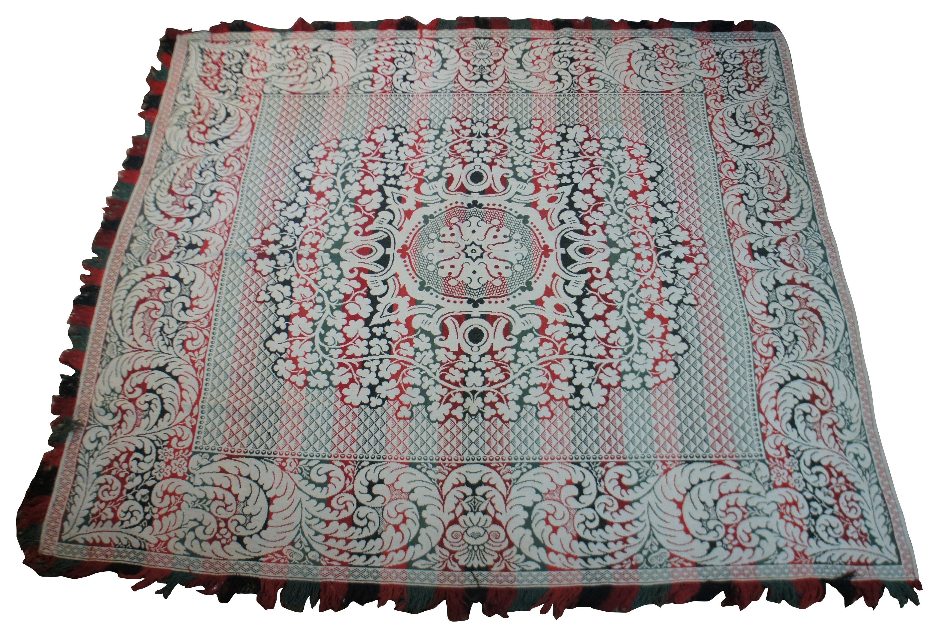 Vintage full or queen size green, red, and white woven blanket with a pattern of swirling leaves and flowers, and a tricolor fringe bordering three sides of the blanket.