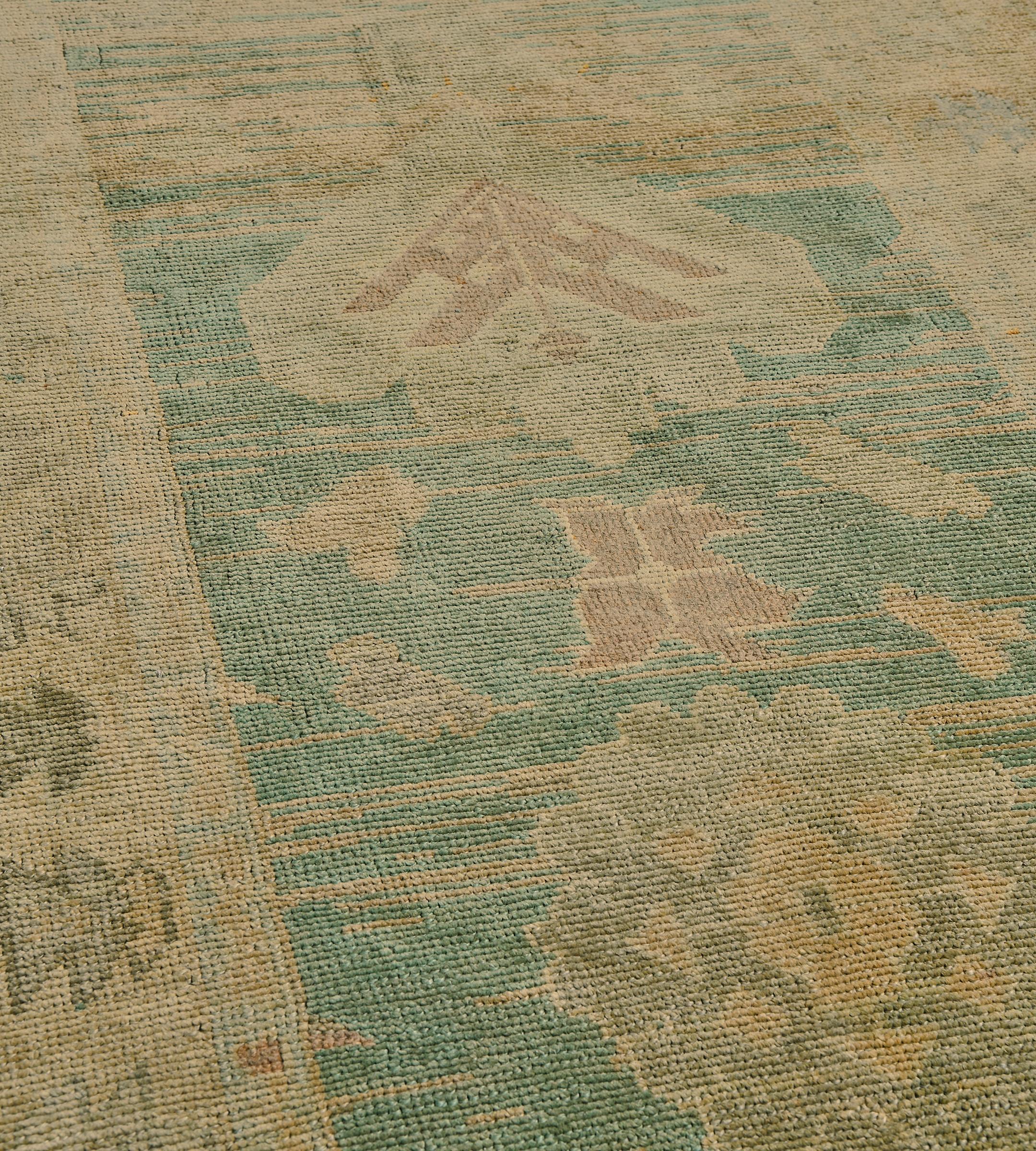 Dieser handgewebte türkische Teppich im Vintage-Stil hat ein waldgrünes Feld mit spärlich gesprenkelten Blättern und Blumenköpfen, mit einer breiten inneren Reihe geometrischer Medaillons und Rosetten, in einer gedämpften beigen Bordüre mit