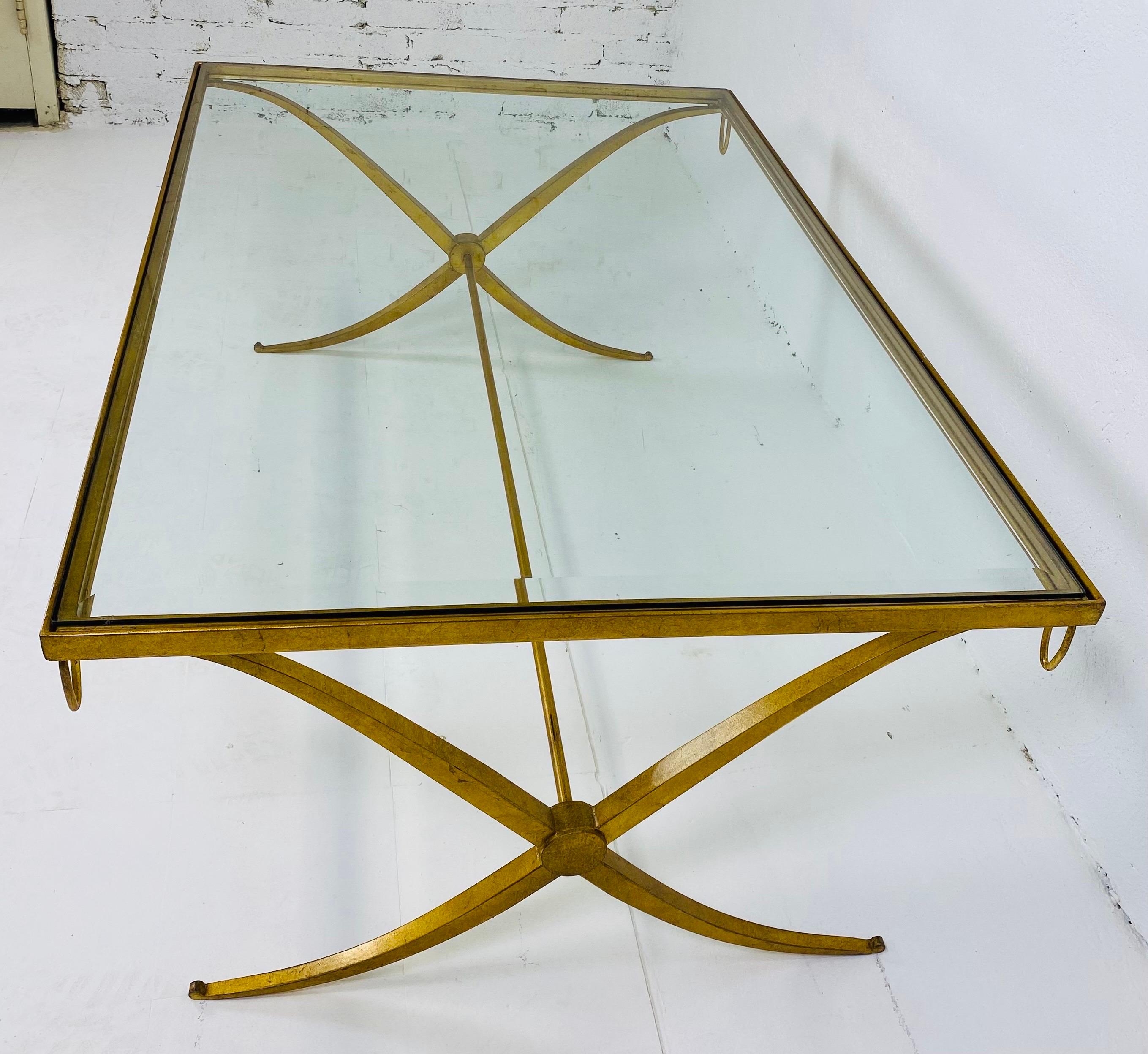This is a late 20th century hand wrought iron gilded cocktail table. The glass on the top of the table has a 1 inch bevel around the entire edge. The cocktail table is in the empire style with a soft curved leg and four rings on each corner, making