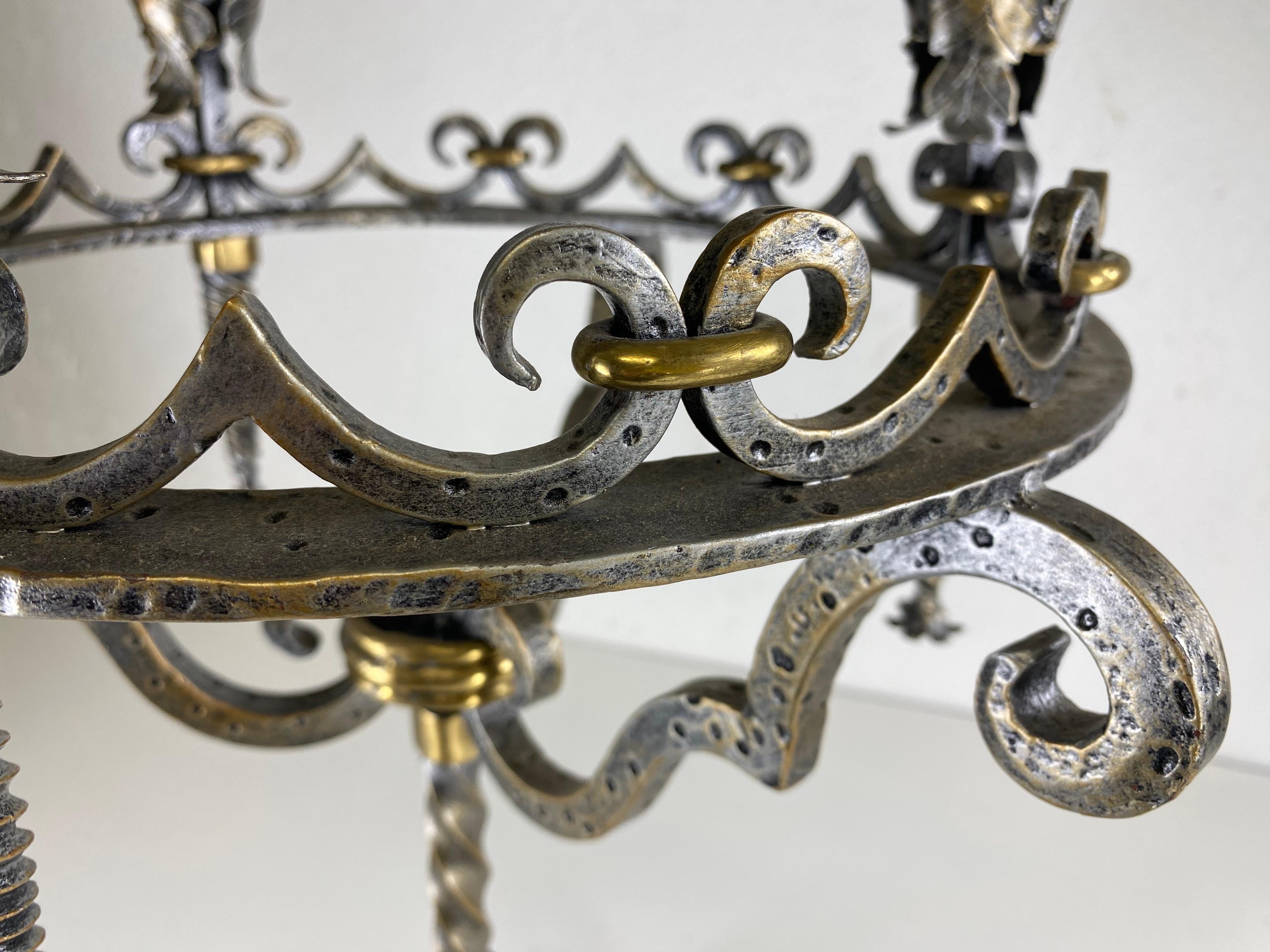 Si tratta di un grande candelabro vintage in ferro battuto in stile gotico revival Questo candelabro è in ferro battuto a mano con dettagli in ottone. Il candelabro ha una superficie in argento lucido anticato. Il candelabro presenta dettagli