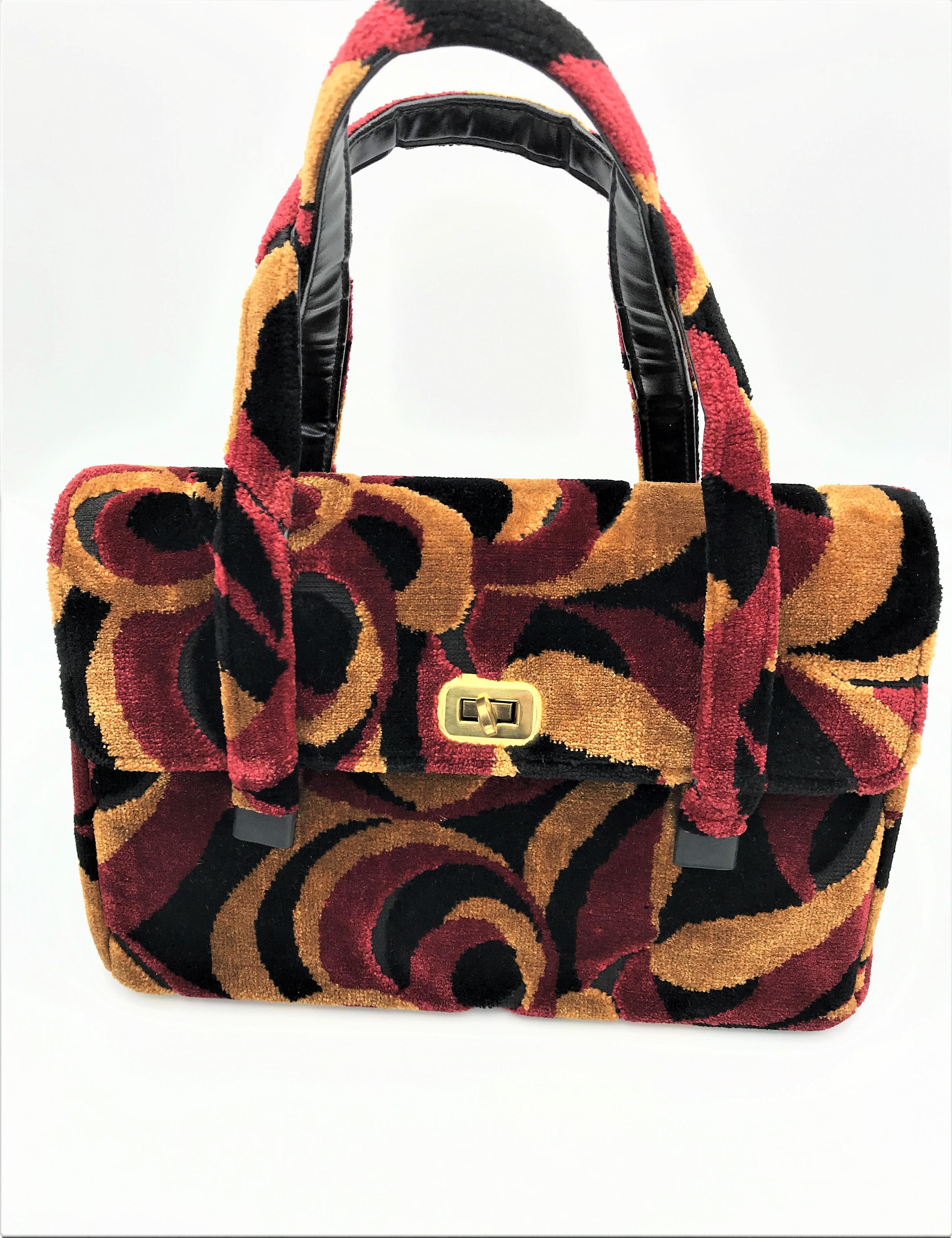 A fun young bag from the USA with 2 handles made of printed velvet. It is lined with black rep on the inside, has a zipper and an open compartment opposite. It is located under the zipper compartment with a gold sticker that says 