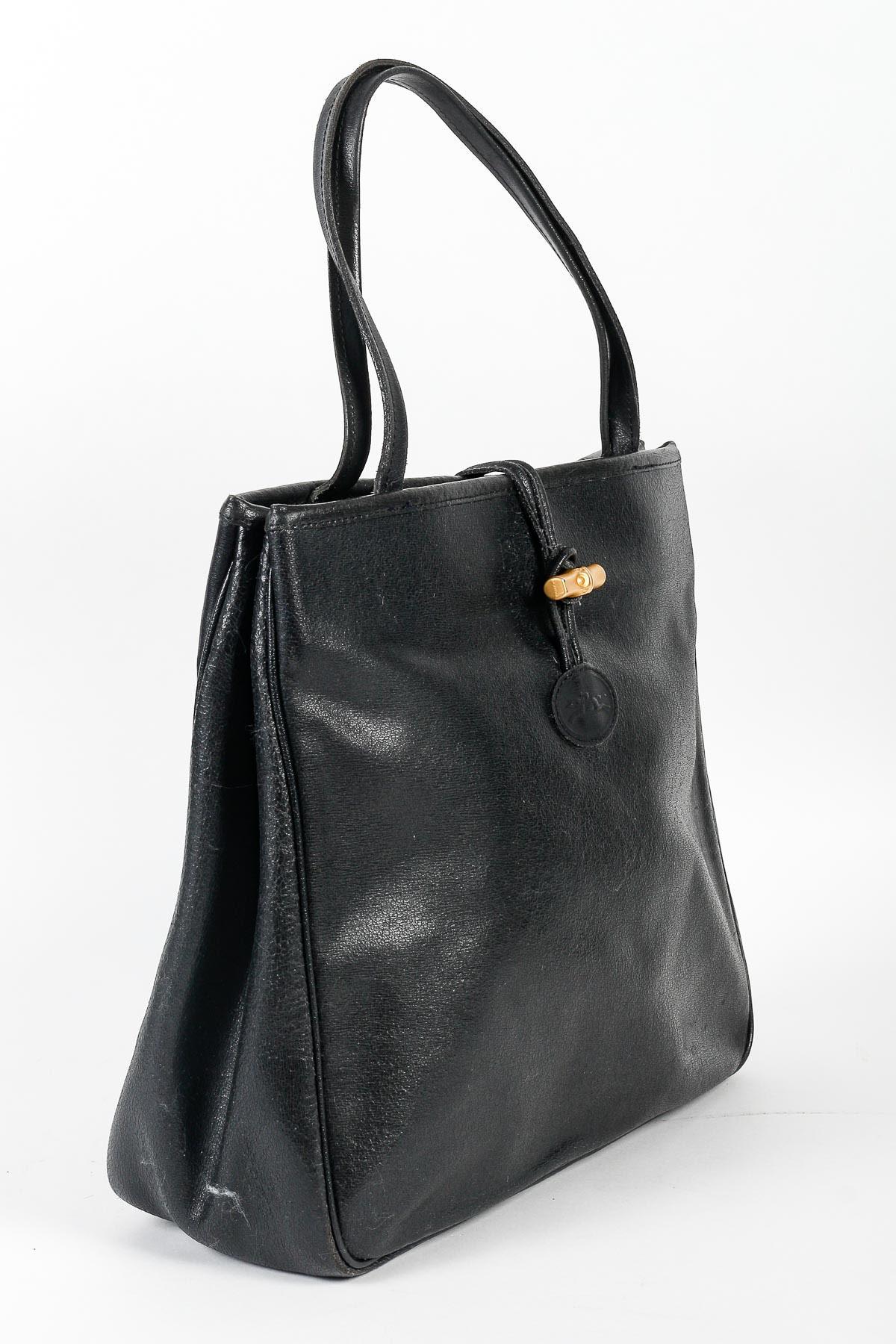 Vintage Handbag, Longchamp, Black Leather, XXth century.

Handbag by Longchamp, black leather, bamboo style gold buckle, leather cracked by time on the front, XXth century.    
h: 29cm , w: 32cm, d: 11cm