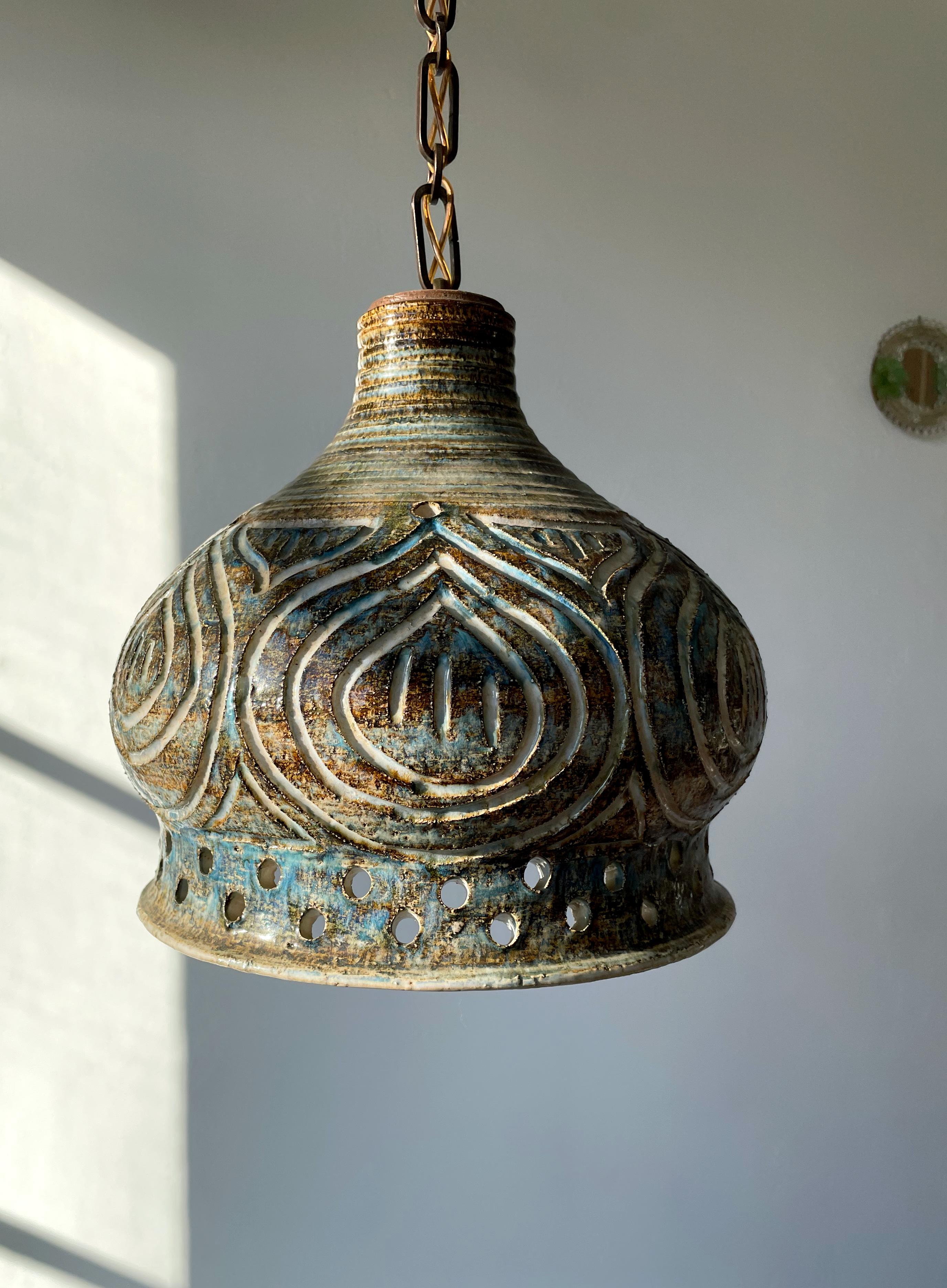Unique handmade ceramic pendant with hand-carved incised organic decorations. Bell shaped body with perforations on the lower and top part for the light to shine through. Glazed with sand, cream, light blue and brown colors. Adjustable 1 m long