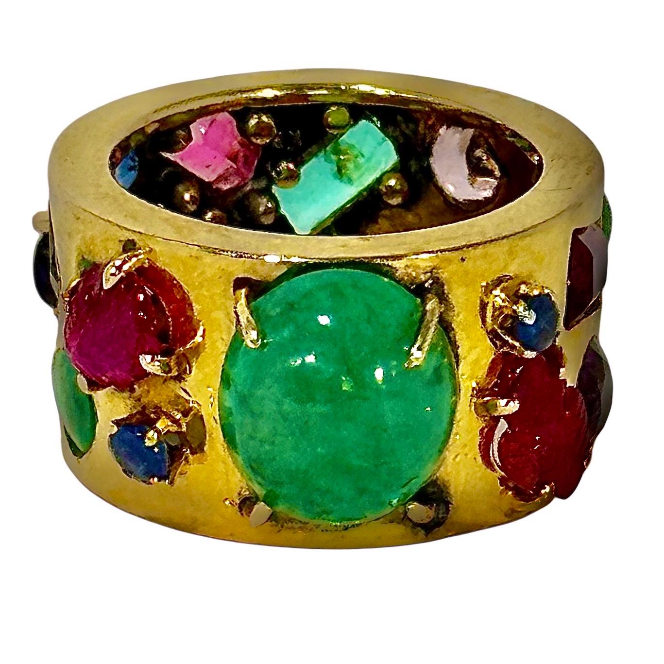 This intriguing and impactful, vintage 14K yellow gold band ring is prong set with a principal natural cabochon emerald weighing approximately 4.00ct surrounded by twenty bezel and prong set faceted and cabochon colored stones ranging from rubies,