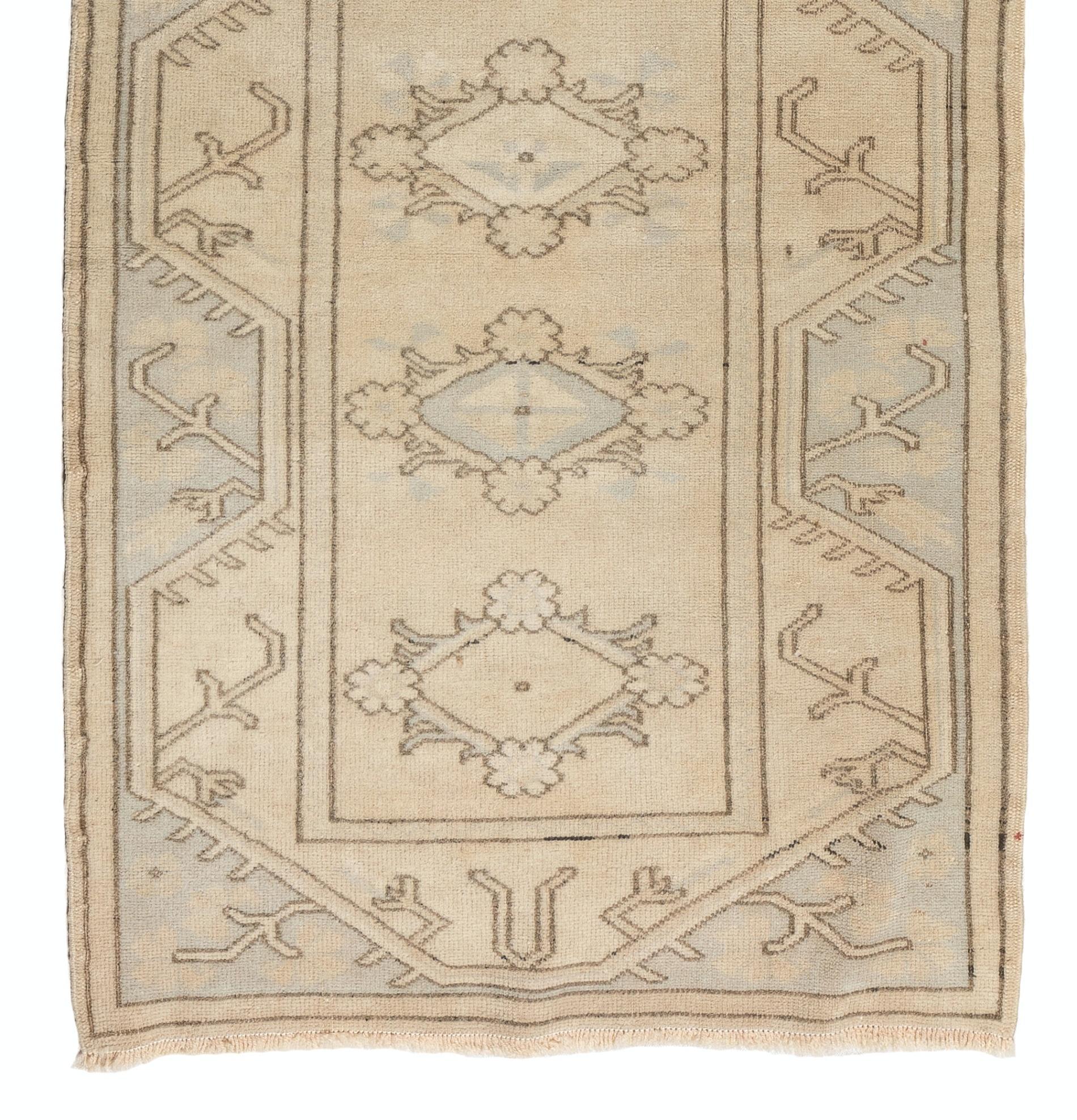 A vintage handmade Turkish runner rug with a geometric design of multiple lozenge-shaped medallions embellished with floral heads as well as angular stem and leaf motifs in sand beige and very light blue. The rug was hand-knotted in Turkey in the