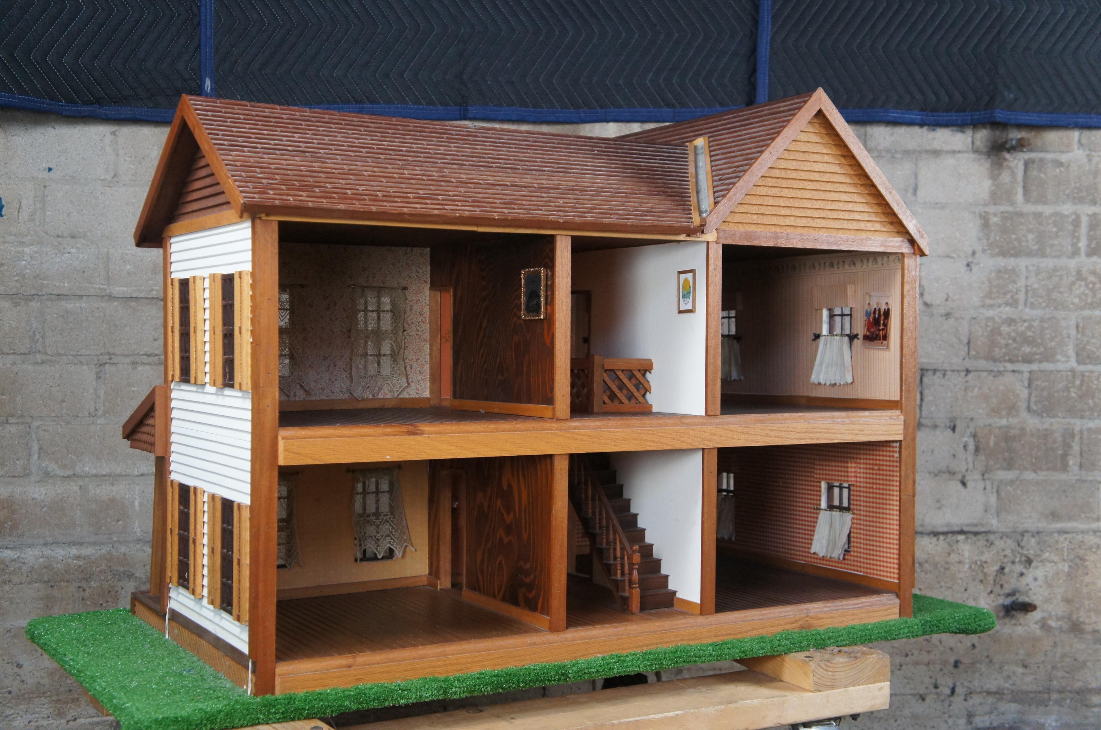 A lovely handmade 2 story 1:12 scale dollhouse. Made from pine with cut moldings, siding, shutters, front porch with turned railings and windows with curtains. The interior has a wood floor, staircase and wallpaper. Mounted to a wooden base with