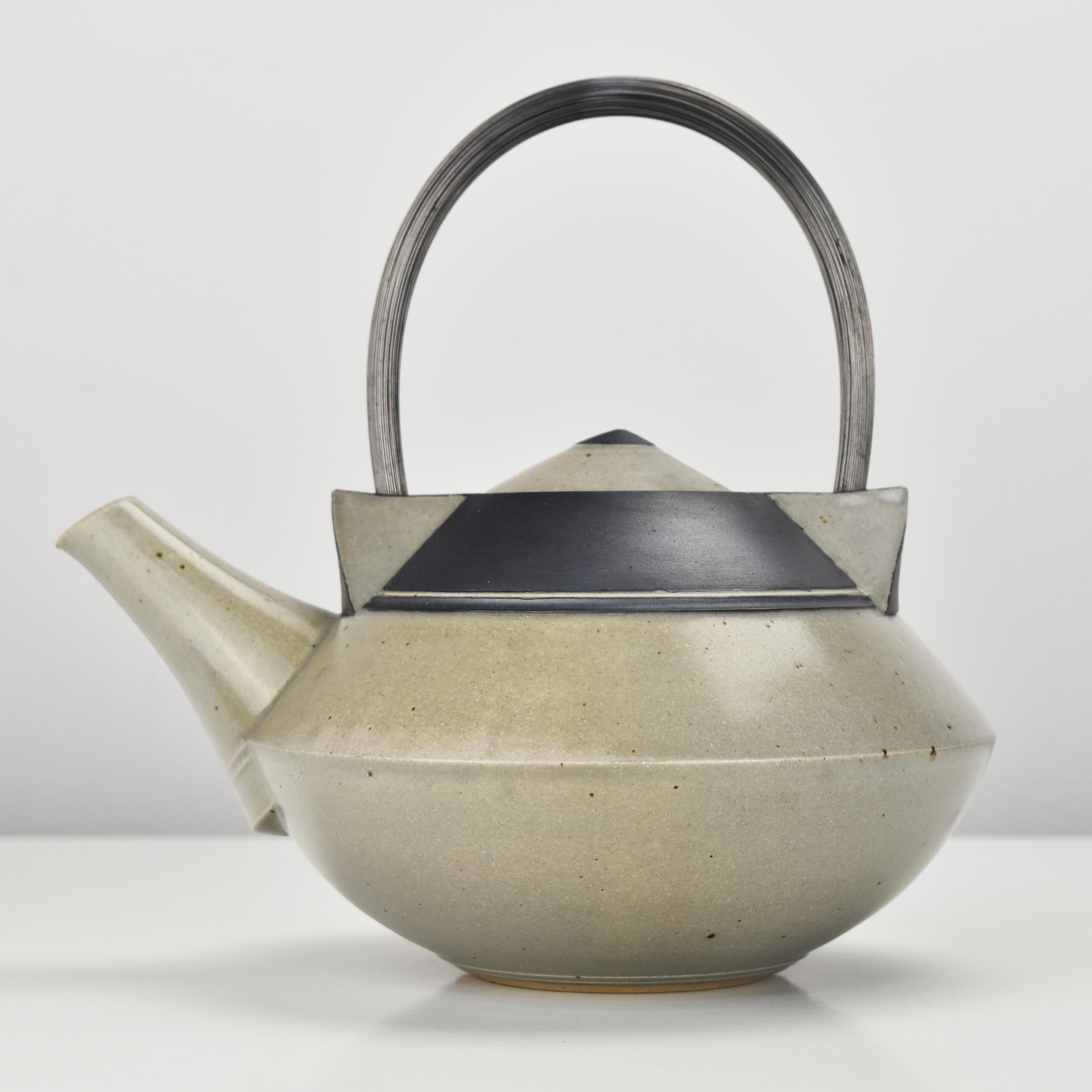 This stoneware teapot is a true masterpiece of modern studio ceramics. It features a dissolved surface glazed in a combination of semi-gloss stoneware with matte black accents. The handle, made of a many of stainless steel wires, is particularly