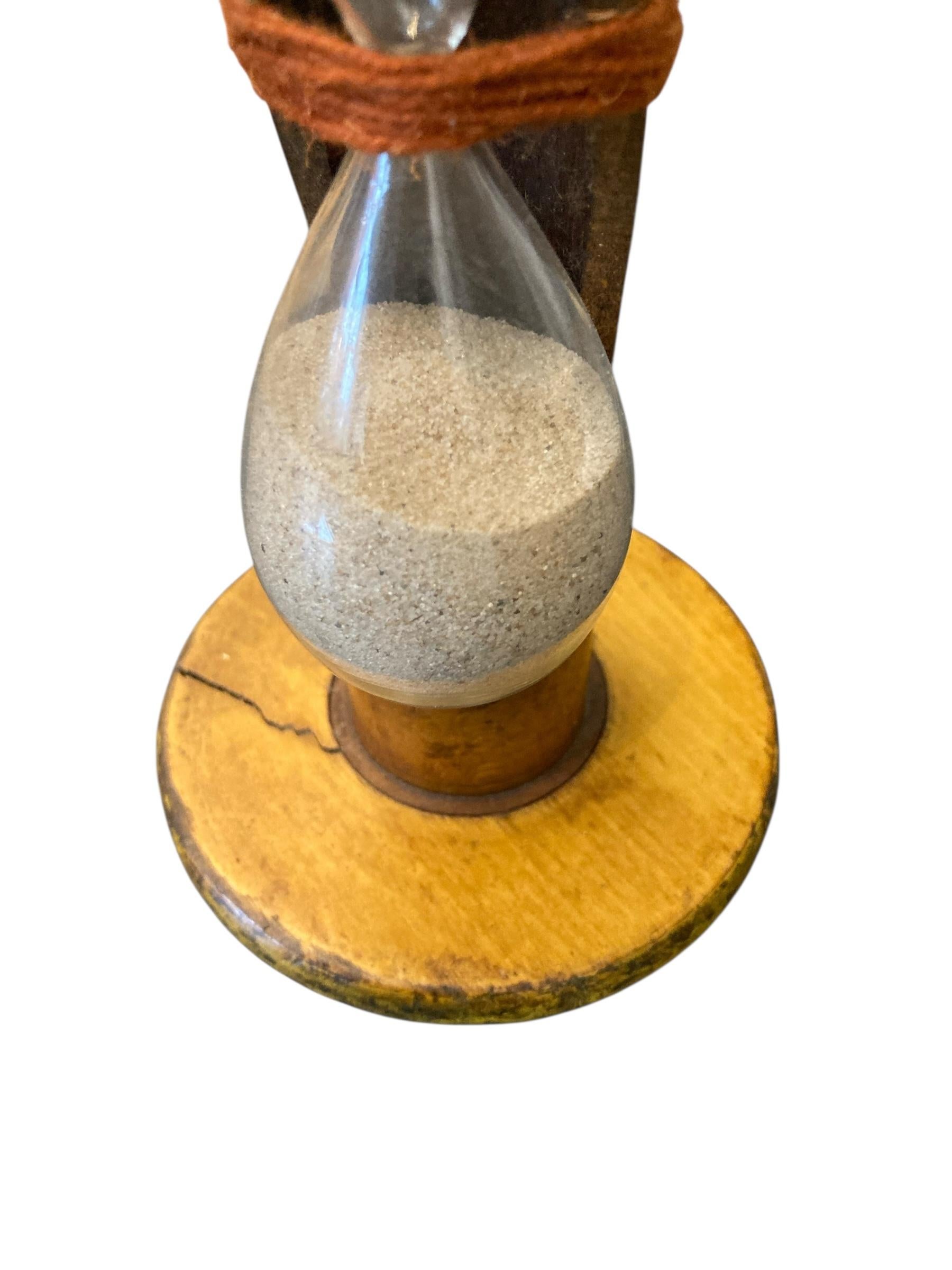 Vintage Handmade Egg Timer Hourglass in Wooden Textile Bobbin Spool 3min Timer. Crafted with precision, the hourglass features fine sand that flows smoothly, symbolizing the passage of time while adding a touch of sophistication to any decor.