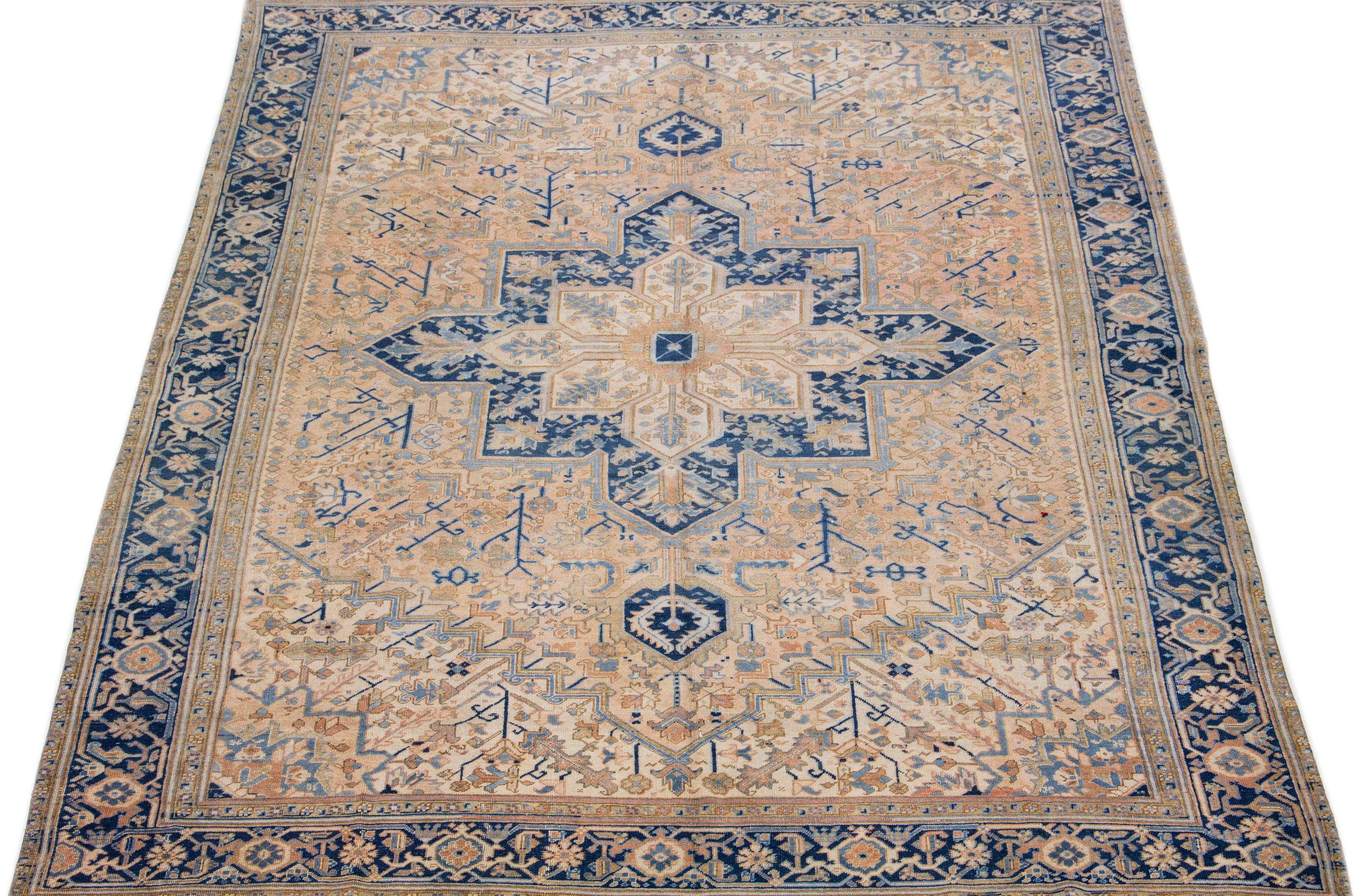 The vintage Heriz rug's hand knotted wool and remarkable medallion design exude Classic elegance and sophistication. The intricate floral motifs in shades of blue and brown, accentuating the soft peach field, lend an alluring touch, making it a
