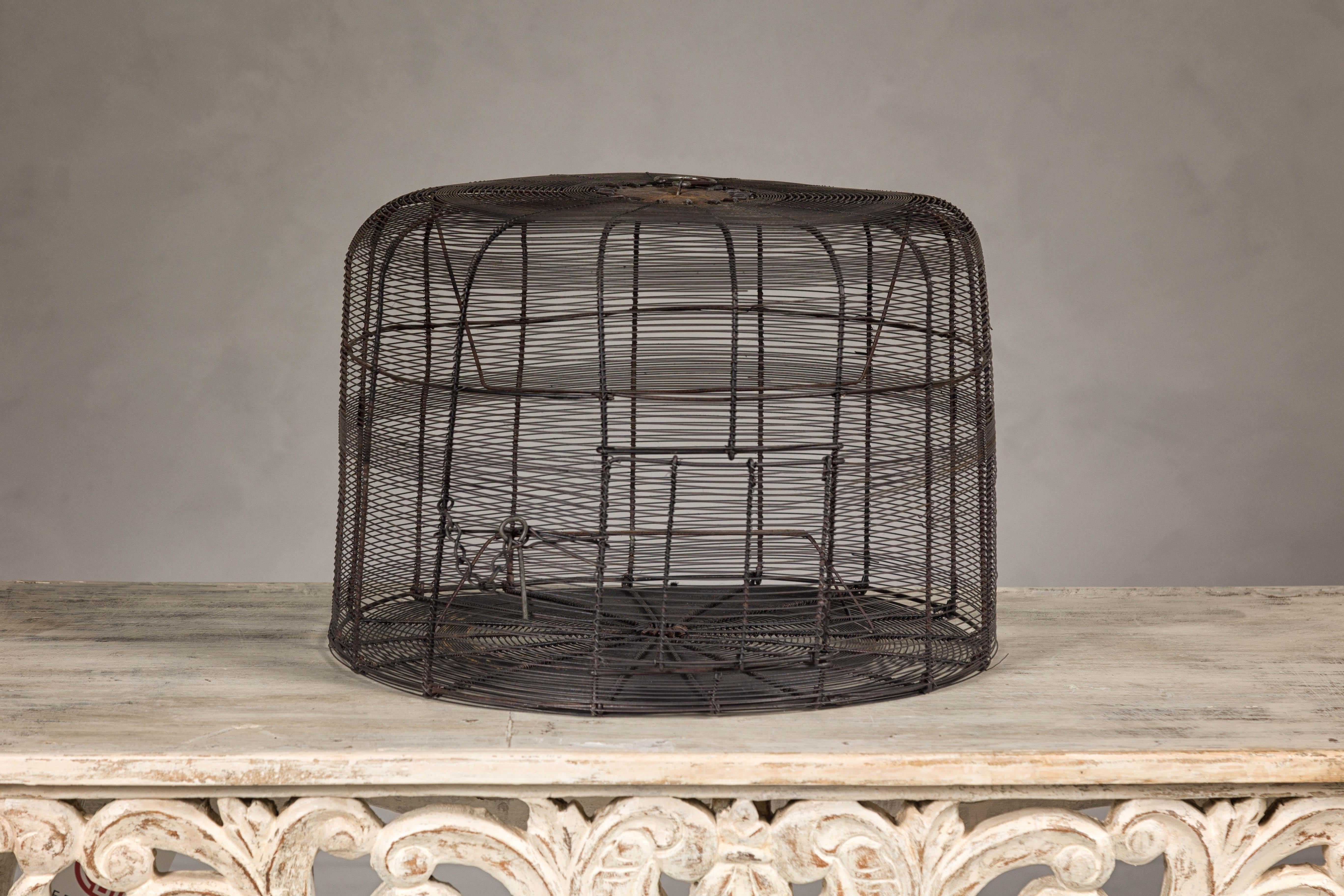 A vintage handmade round shaped metal birdcage with rustic character. This charming vintage handmade round-shaped metal birdcage exudes rustic character and timeless appeal. The birdcage, with its distinctive lopsided design, showcases a dark patina