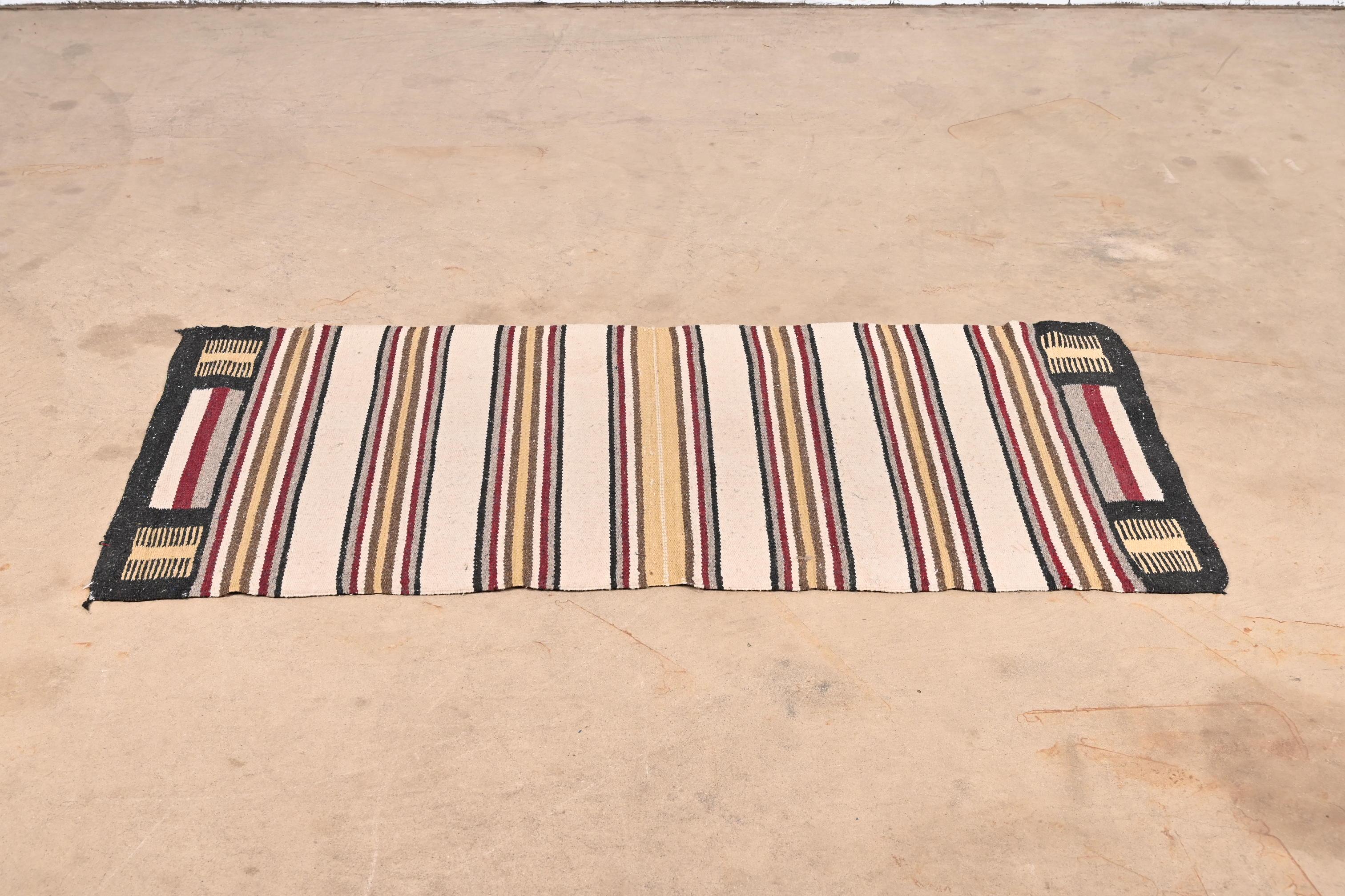 A gorgeous vintage handmade Navajo flat weave wool rug

USA, Mid-20th Century

Striped design, with predominant colors in burgundy, yellow, brown, black, and ivory.

Measures: 28