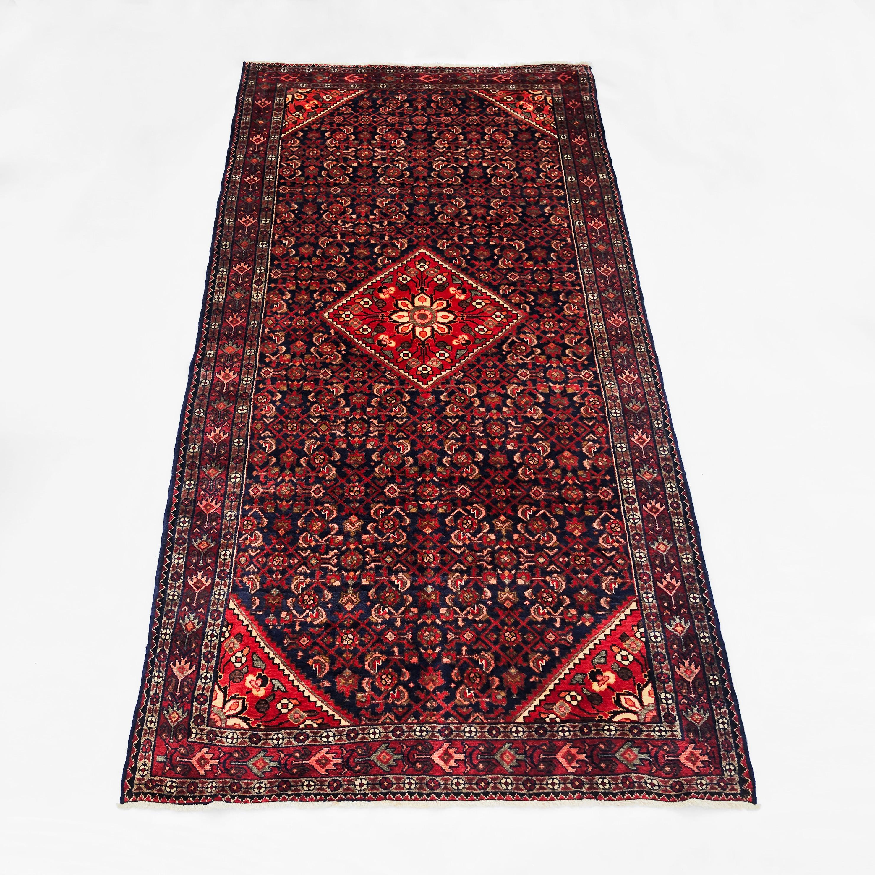 Ce tapis en laine fabriqué à la main à Hosseinabad, en Iran, présente un motif Herati complexe dans des tons profonds de rouge et de bleu. Le motif Herati est un motif persan traditionnel, que l'on croit basé sur des motifs Farahan plus anciens,