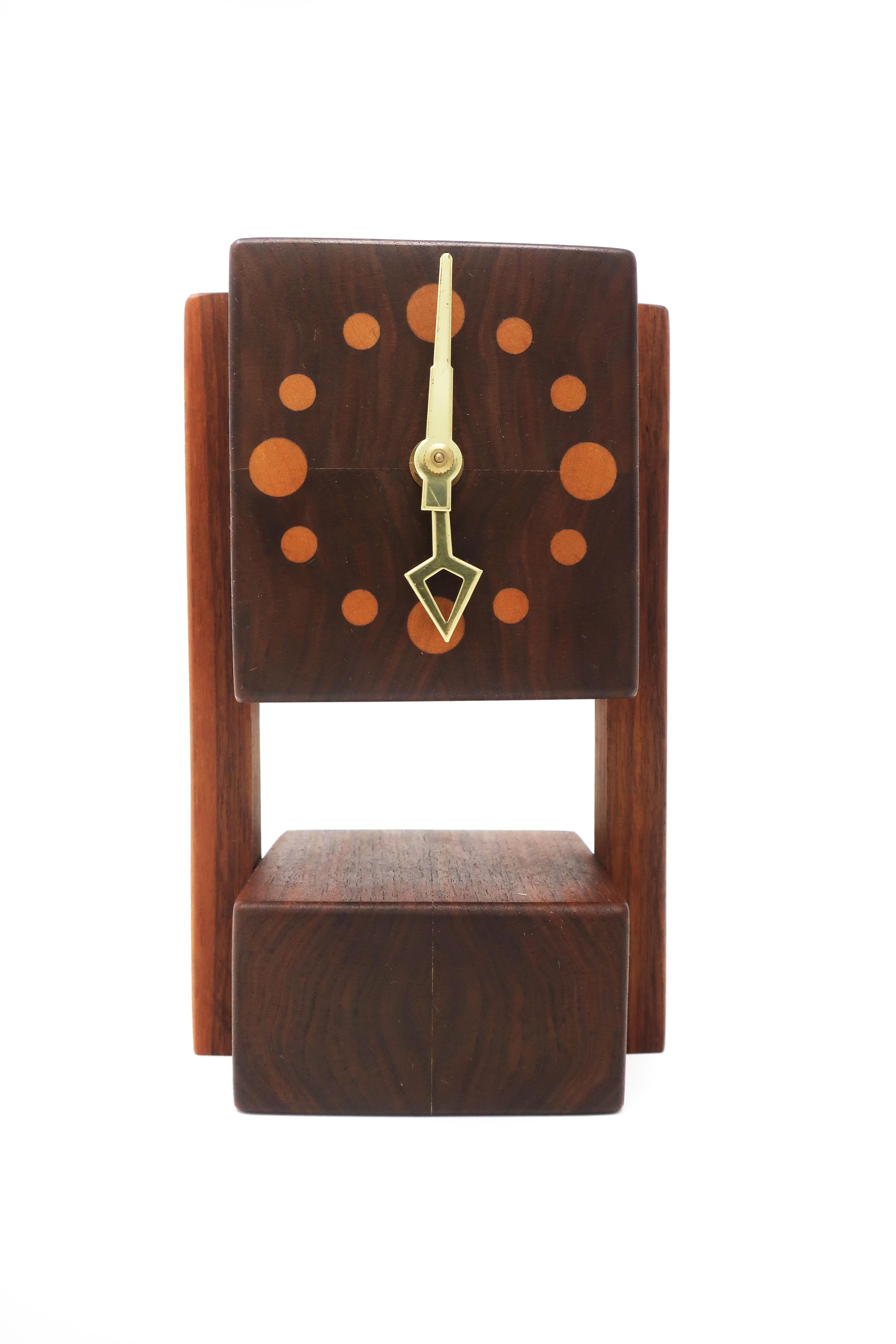 A lovely vintage wooden desk or mantle clock. The base, supports, and housing for the movement are teak, with contrasting lighter wood inset circles serving as the clock’s numbers. Front opens to reveal the clock’s movement.

In very good vintage