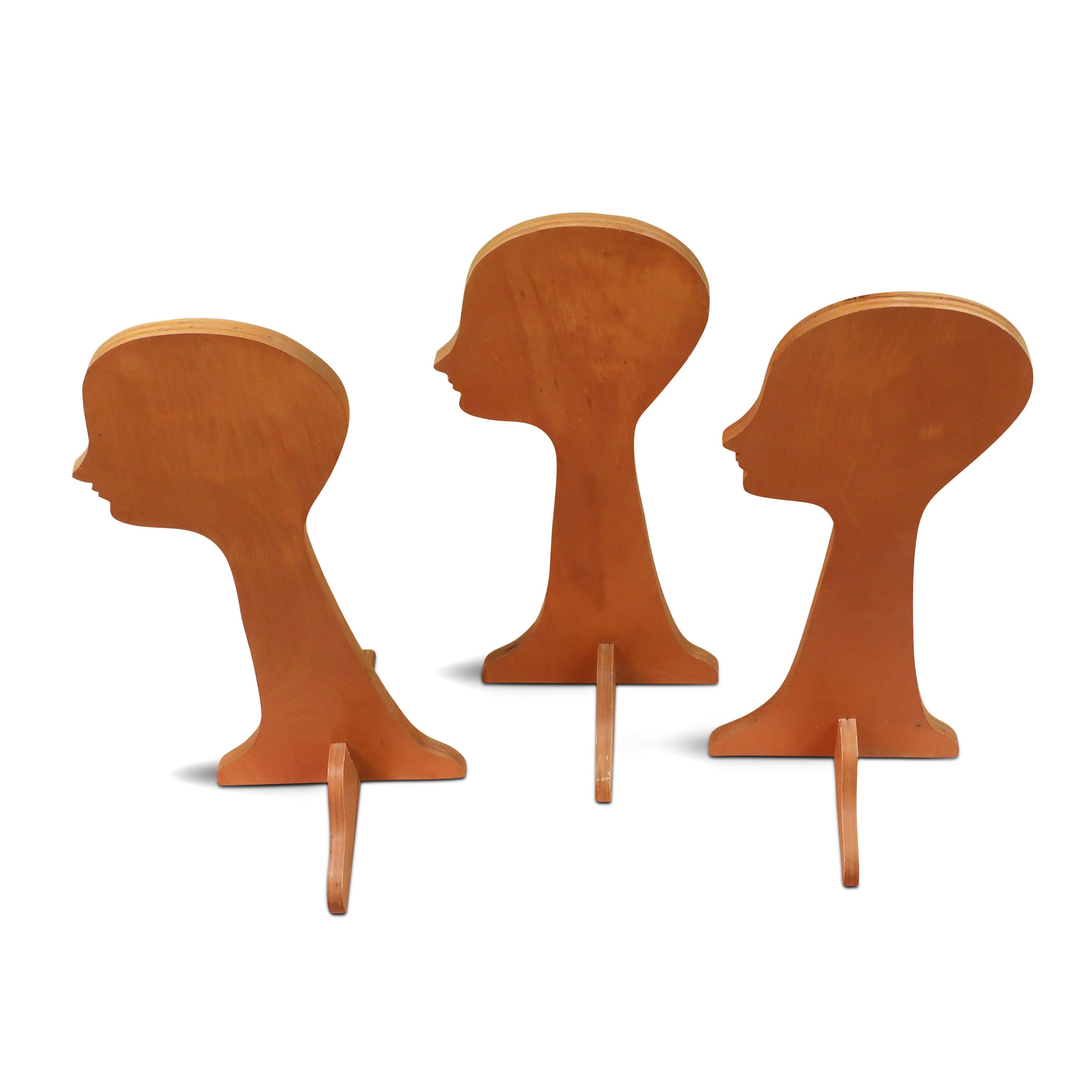 A set of three vintage mid-century handmade hat stands.  Constructed from plywood to resemble a head and face in silhouette, each sits on a plywood x-base.  Made for a Long Island, New York milliner in the 1940s or 1950s to display their wares and