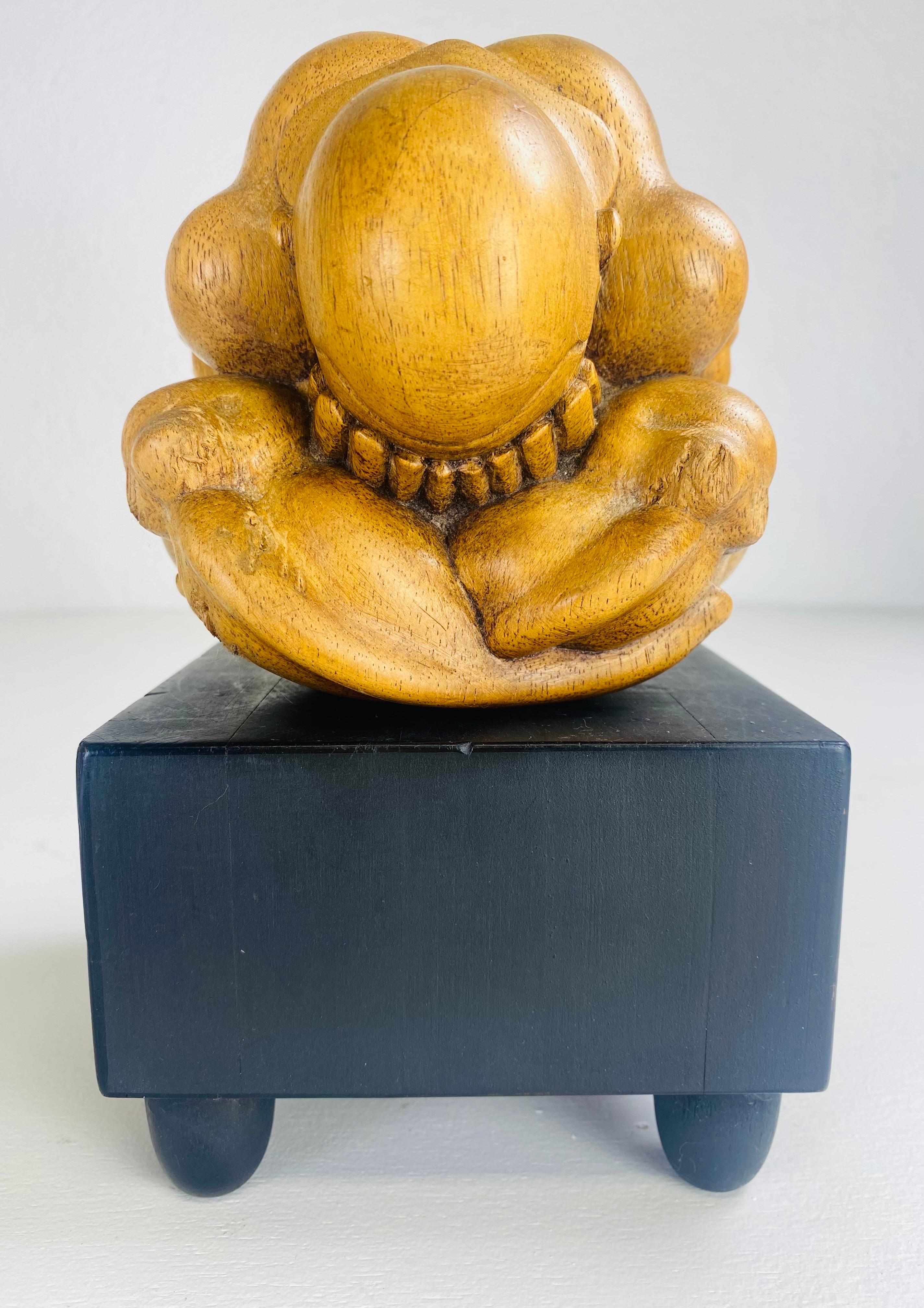 This is a handsome handcrafted male figure standing on a black pedestal. This hand carved figure is uniquely carved into a ball. The sculpture is a man folded over with his head in his hands. This carving is Asian circa 1980.