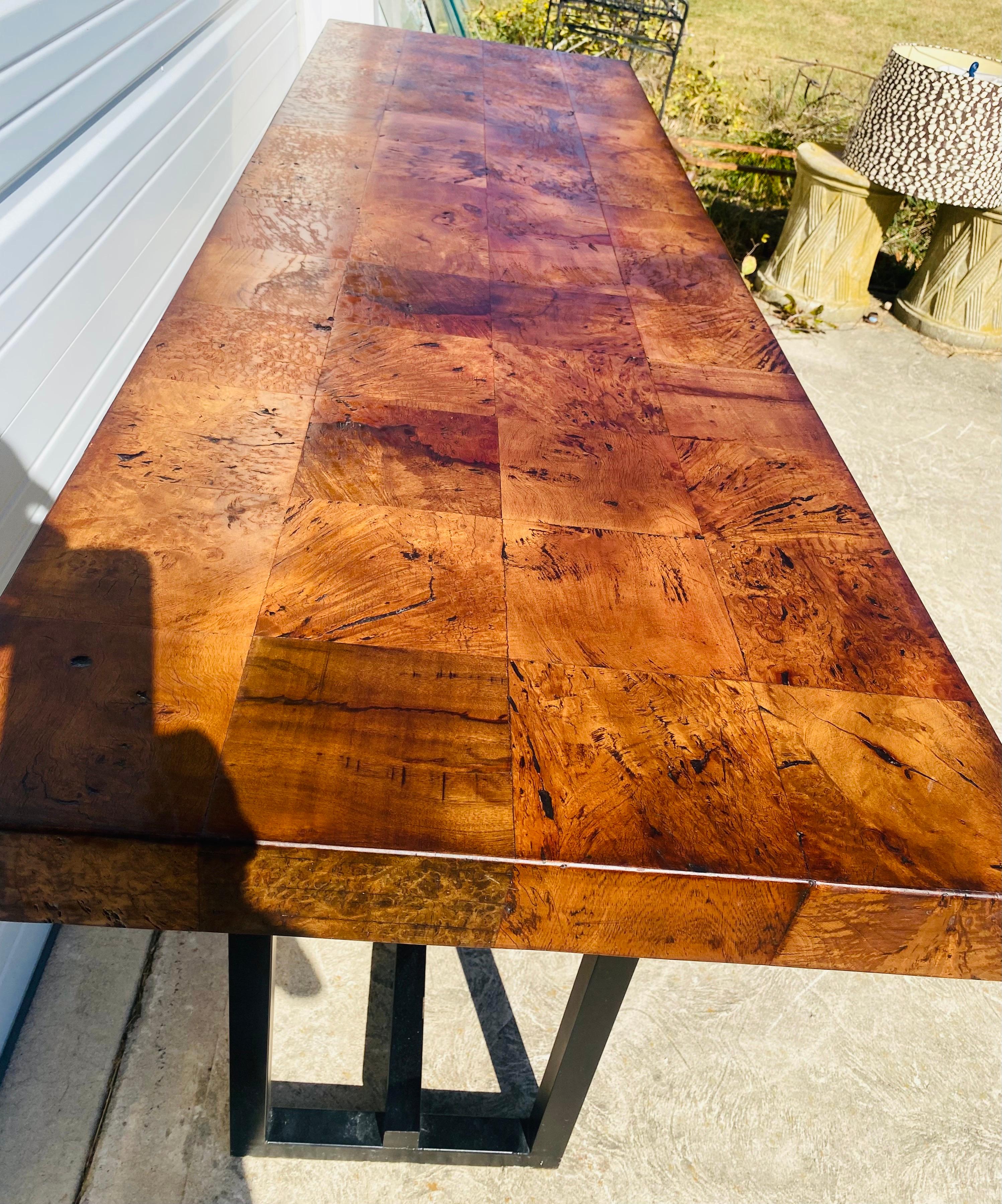 This is a handsome vintage burled walnut console. This console has a black industrial modern base with a burled walnut top. The Amber colored burled walnut top is in a patchwork parquet design. This table was American made circa 1990.