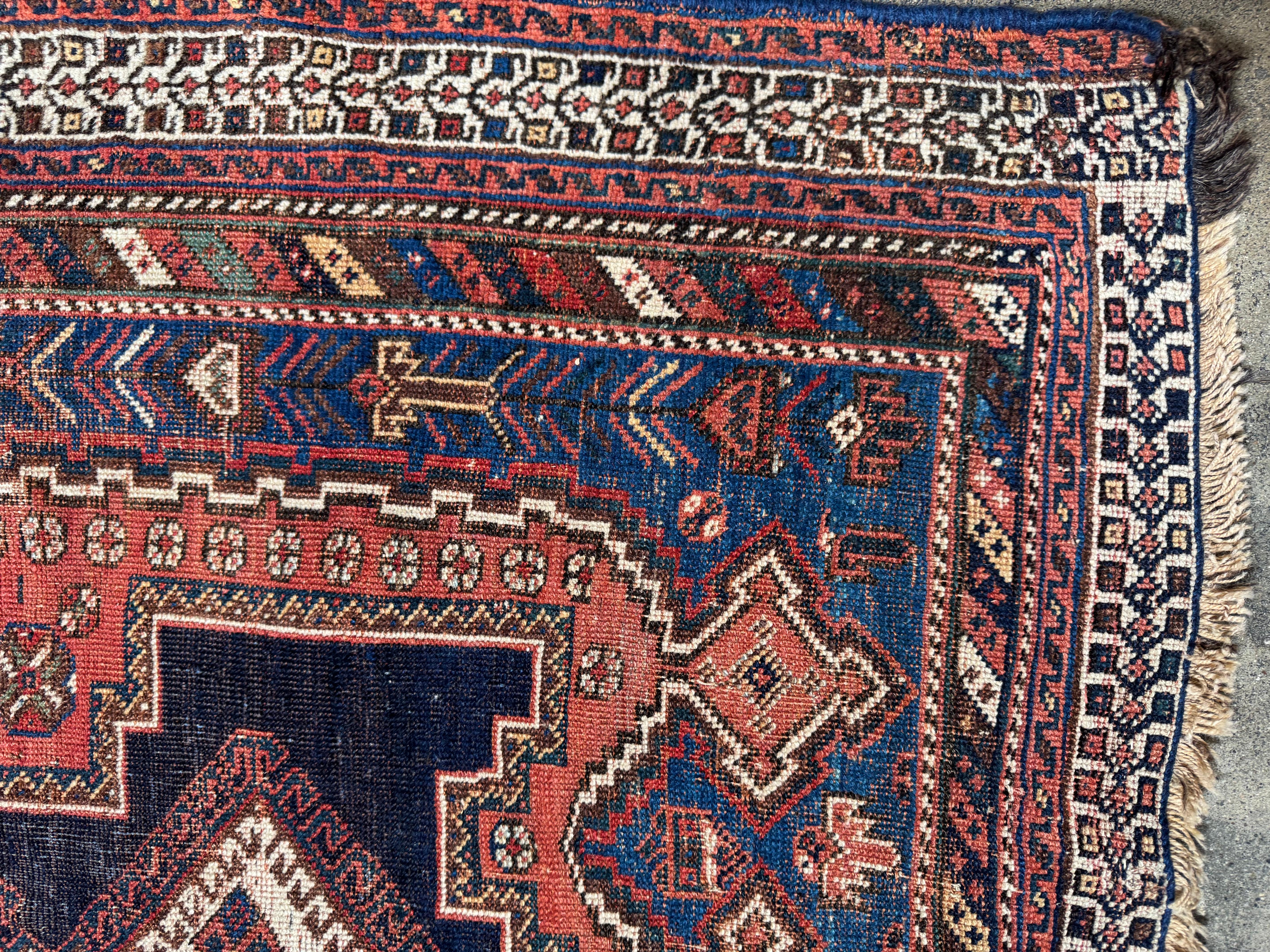 Questo tappeto vintage Afshar è uno splendido pezzo tessuto a mano che presenta un ricco disegno tribale con audaci medaglioni geometrici, bordi intricati e una sorprendente tavolozza di colori blu scuro, rosso mattone e avorio. L'artigianato mette