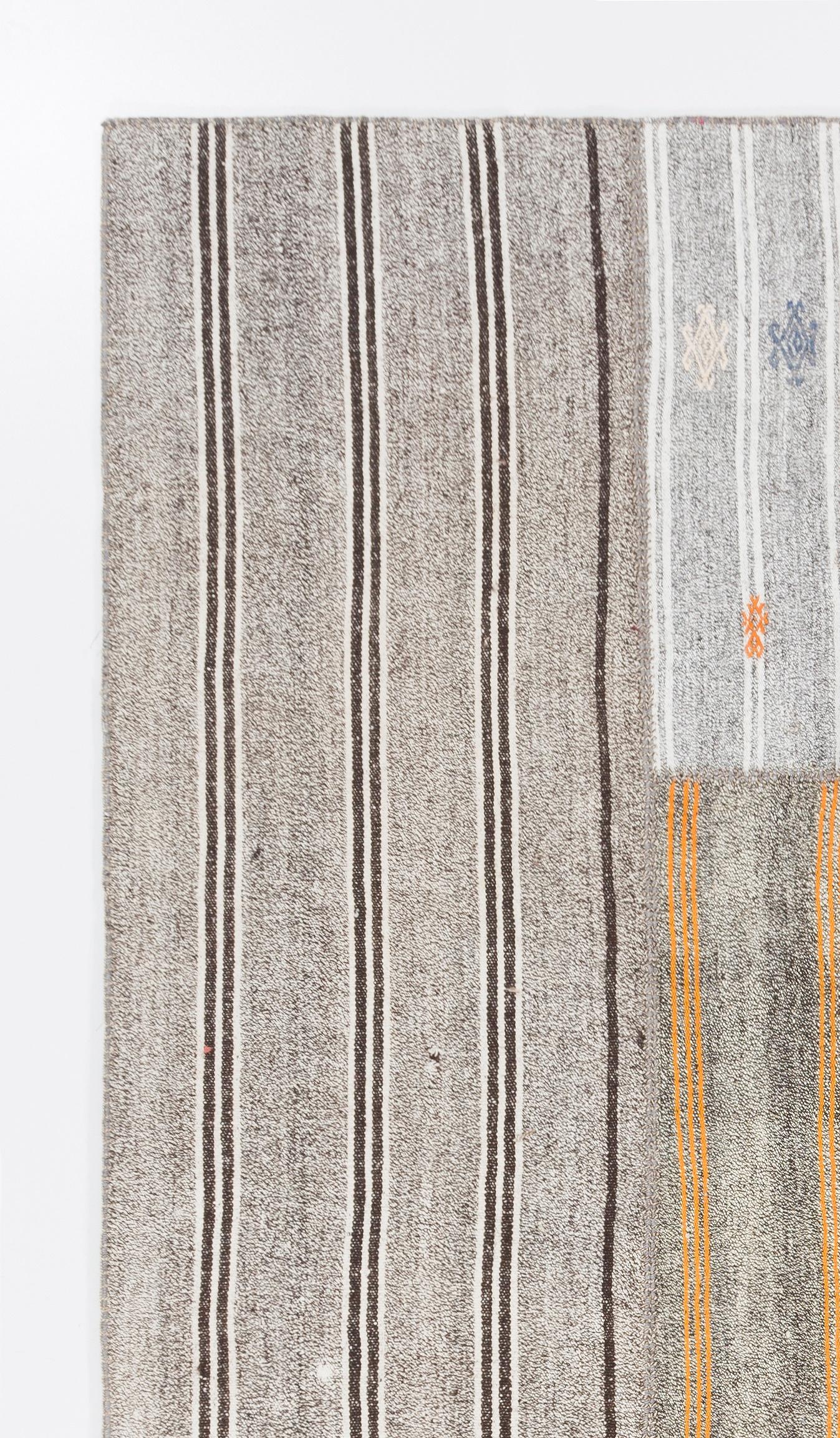 A simple, minimalist Turkish flat-weave/kilim patchwork rug made up of hand-woven and hand-stitched vintage kilim pieces that feature stripes and burdock motifs against the speckled looking texture of the background, in brown, gray, ivory and