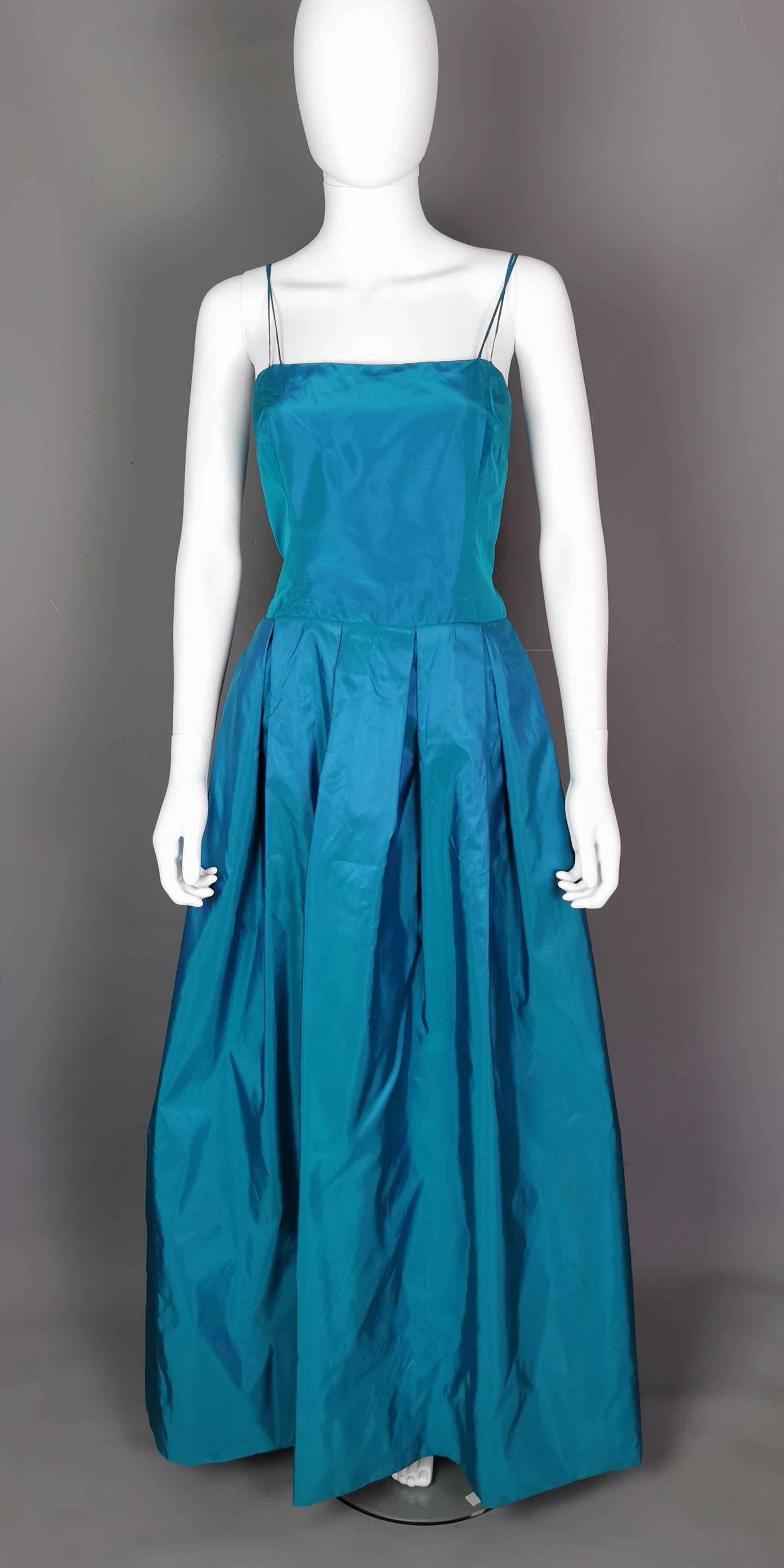 An incredible vintage two piece dress by Hardy Amies.

Made in a vibrant slightly two tone blue / green shot silk taffeta the set comprises of a long length evening gown and a matching bolero type jacket.

It is a teal blue with a metallic green