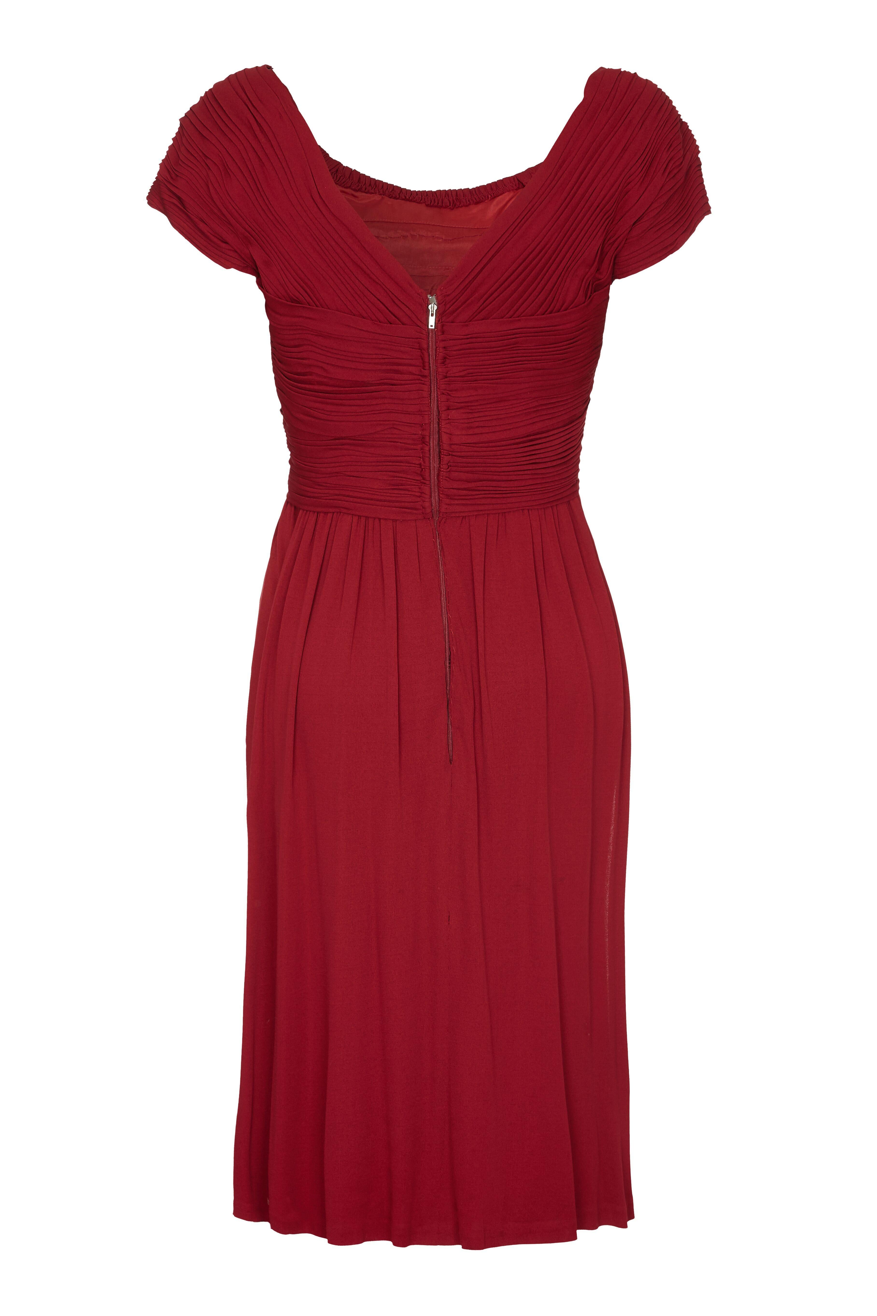 This gorgeous 1950s vintage Harrods boutique dress in deep burgundy showcases some exquisite tailoring with unique pleating on the bodice and sleeves. The simple line of the dress with its soft scoop neckline and cap sleeves is juxtaposed with