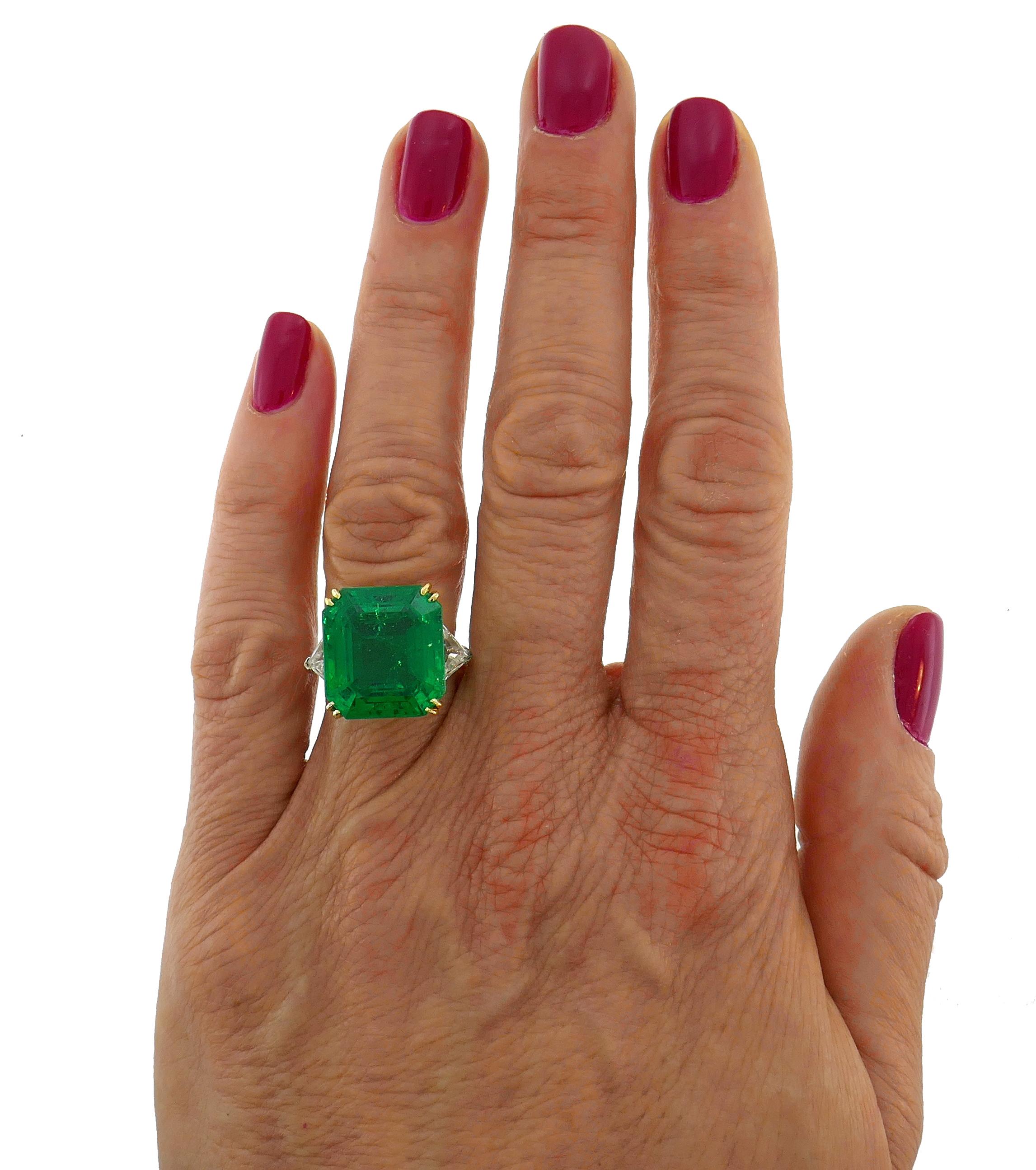 Stunning three-stone platinum ring created by Harry Winston. The ring features an amazing color with fascinating glow 14.04-ct Colombian emerald flanked with two trillion cut diamonds. The emerald measures 15.39 x 14.16 x 9.16 mm and comes with two