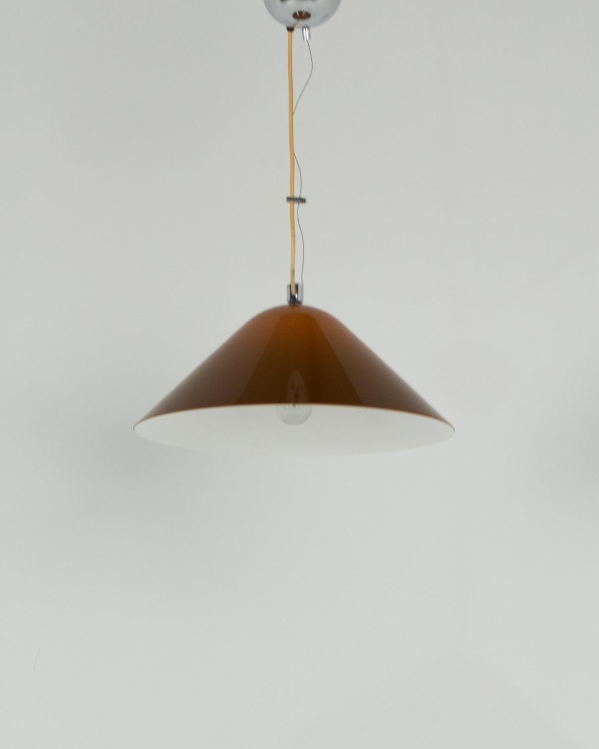 Questa straordinaria lampada a sospensione di Harvey Guzzini per Meblo, risalente agli anni '70, incarna l'iconica sensibilità del design italiano dell'era moderna di metà secolo. Caratterizzata da un elegante paralume conico in acrilico marrone