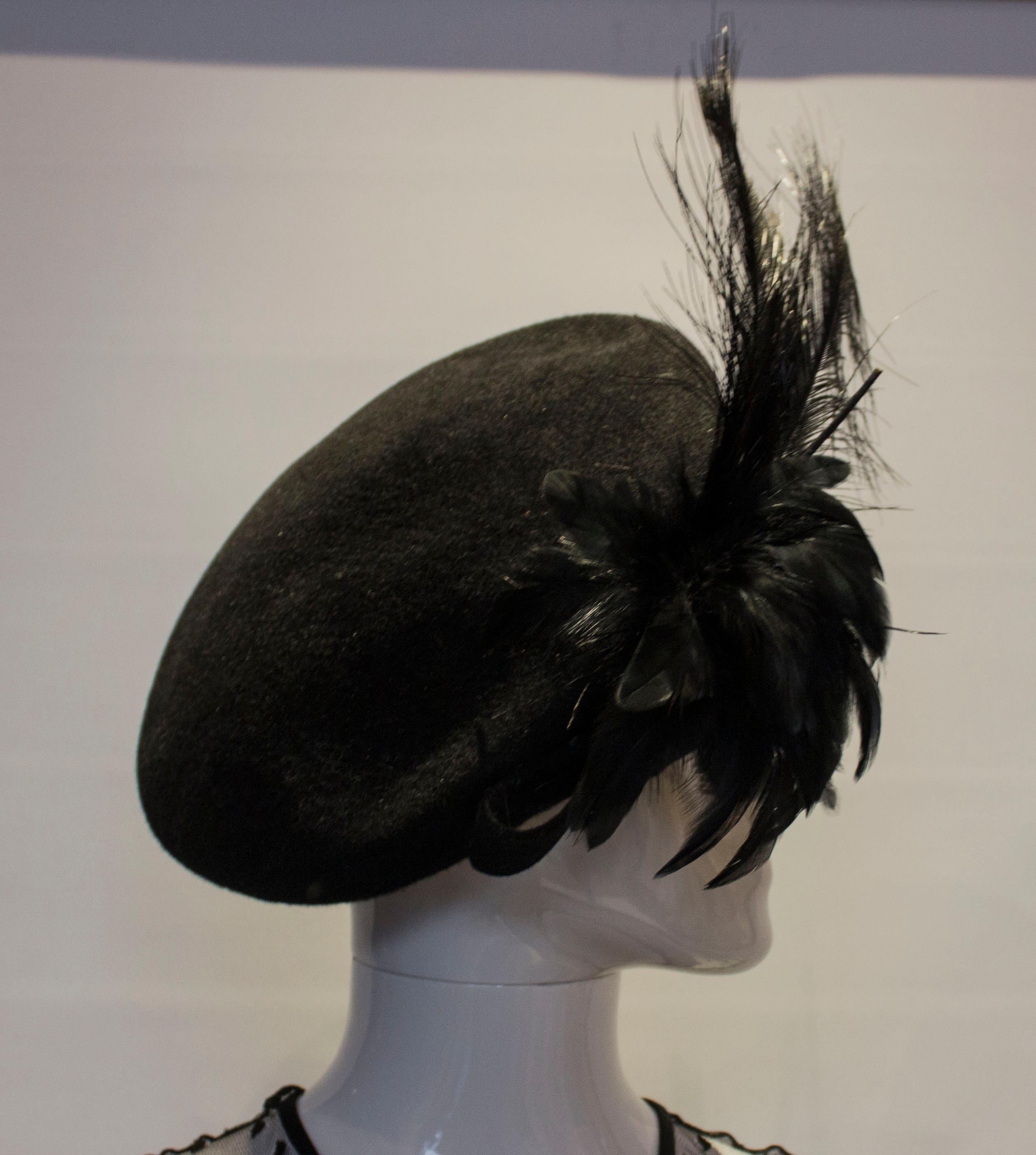 A chic hat for the festive season . In black felt with a graduated ,sloping crown, the hat has a black felt bow and feather detail. The inner circumference is 23'', and the height is 3 1/2''.




