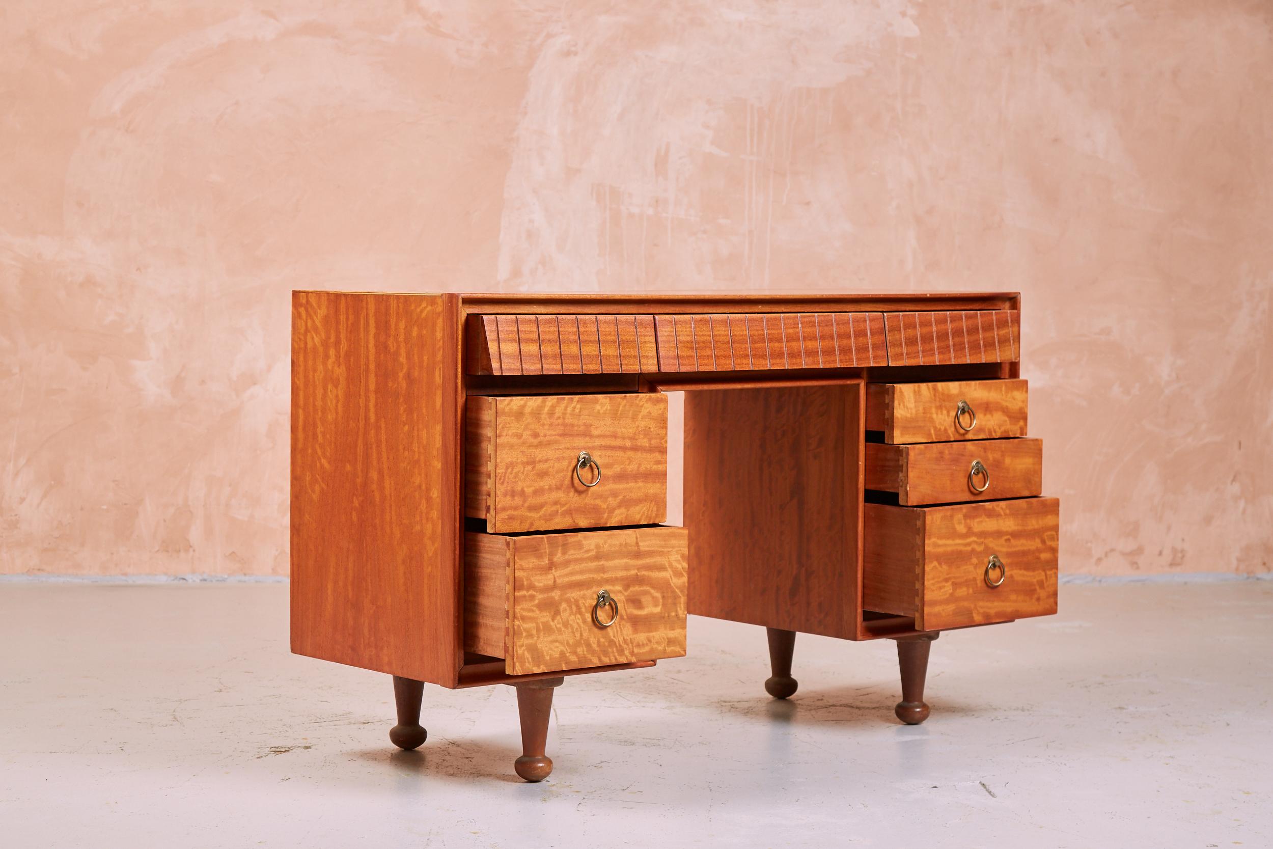 A vintage 1950s dressing table which can also be used as a desk or sideboard, designed by AJ Milne for Heals. The Satinwood veneer has a unique shimmering finish. The piece consists of a row of three shallow drawers across the top along with deeper