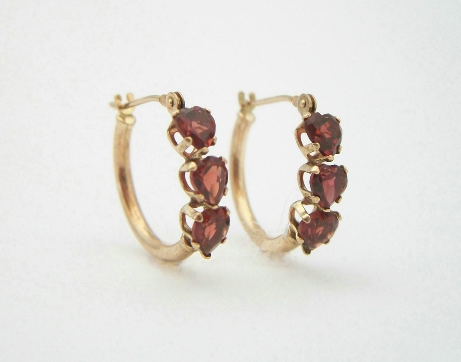 Vintage pair of heart shaped Cubic Zirconia garnet and 10K yellow gold hoop earrings - featuring three prong set CZ garnets to each hoop - signed on each hoop wire (unidentified maker - see last photo) - United States - circa 1980's.

Excellent