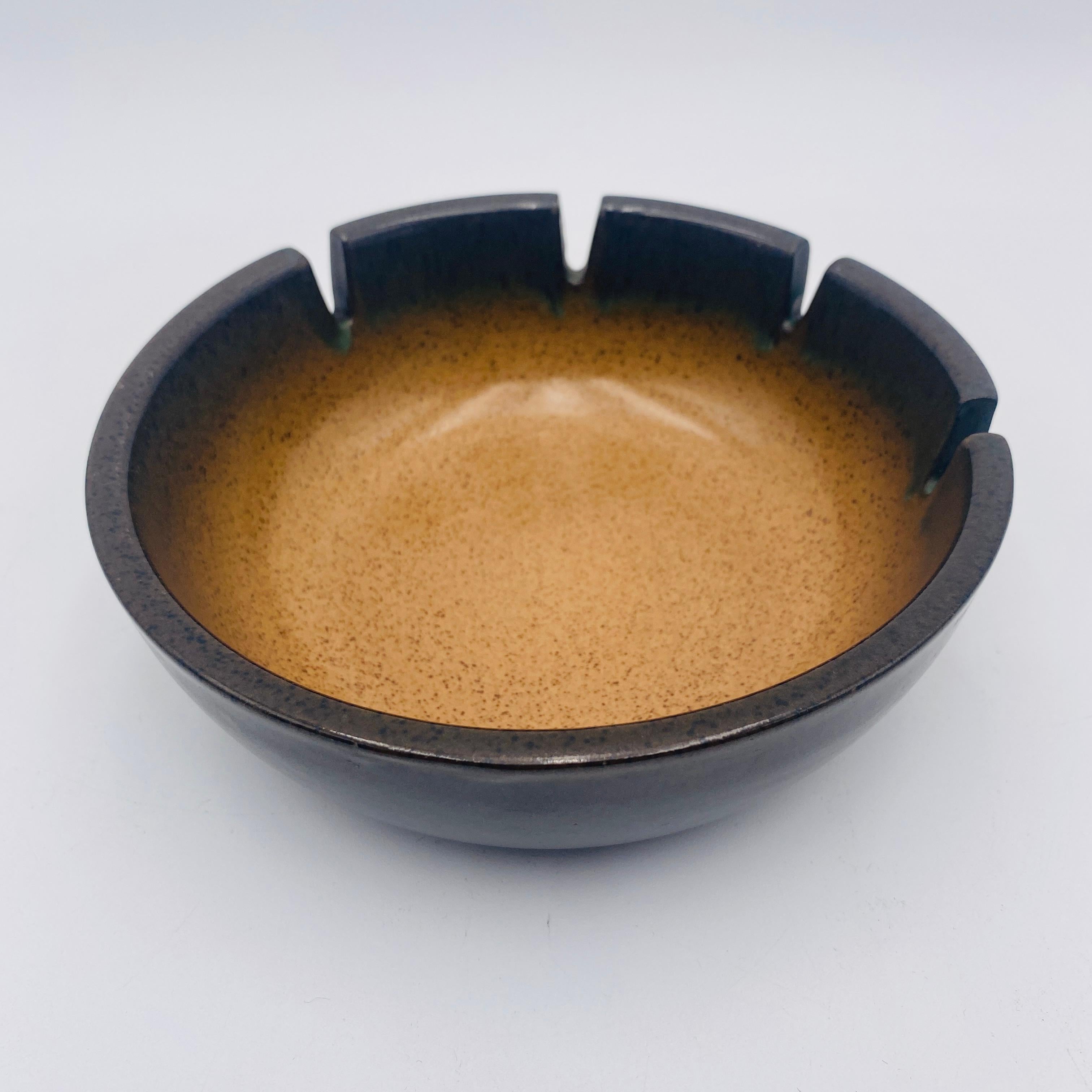 Cenicero de cerámica esmaltada de Heath Ceramics, c.1960, EE.UU. El cenicero presenta un esmalte moteado exterior marrón oscuro que cambia a un esmalte moteado tostado en el interior. Hay cuatro ranuras para cigarrillos. También puede utilizarse
