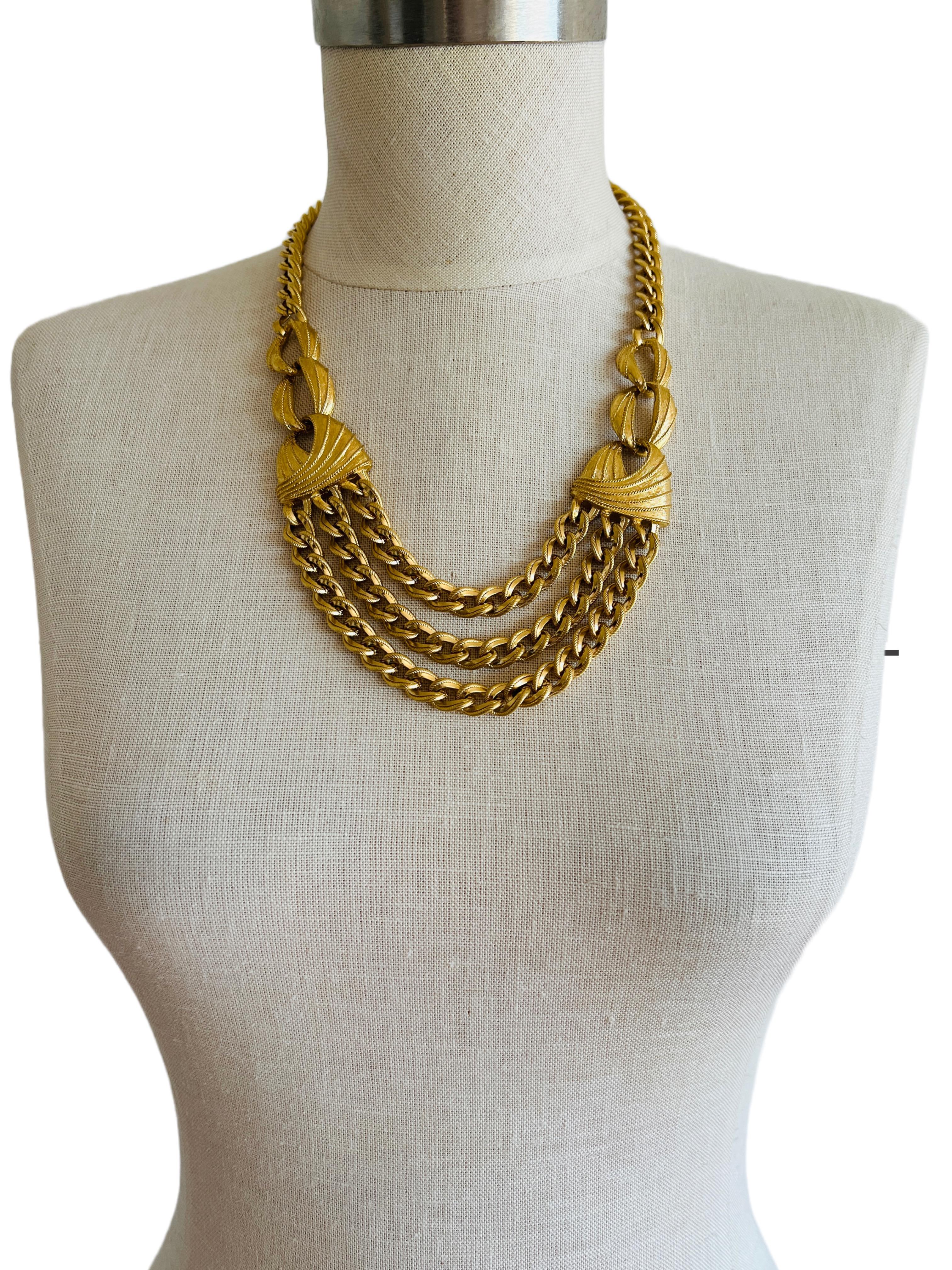 This weighty necklace showcases a blend of classic charm and modern elegance. At its heart lies a trio of curb chains, creating a tiered effect that drapes elegantly across the collarbone. Each chain is composed of flat, closely-set cable links that